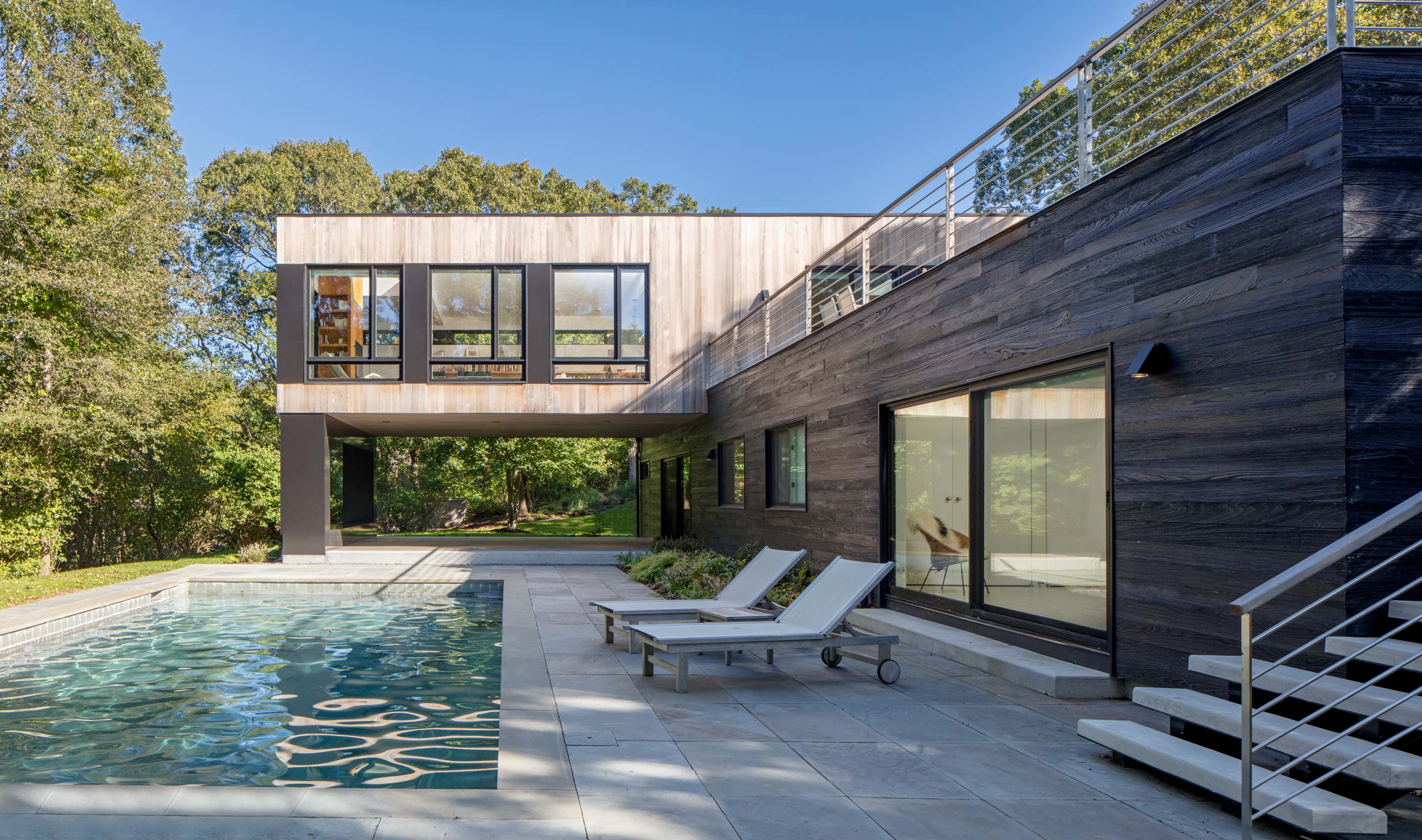 Poolside of Bridgehampton House by Specht Novak Architects featuring cantilevered second floor and wood-paneled exterior. Shot by Taggart Sorensen.