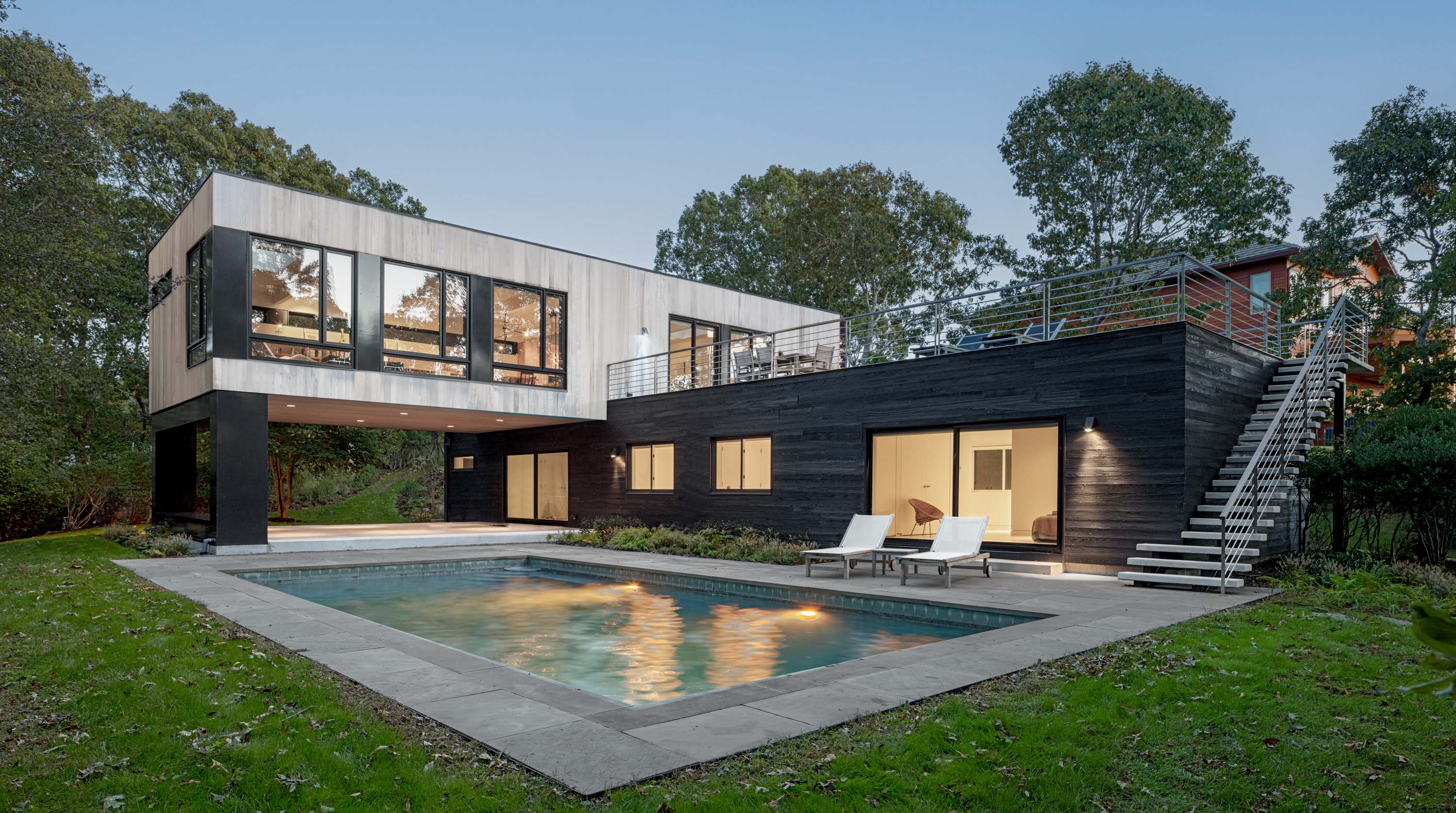 Exterior of Bridgehampton House by Specht Novak Architects showcasing utilitarian materials, roof terrace, pool, and industrial exterior staircase. Shot by Taggart Sorensen.