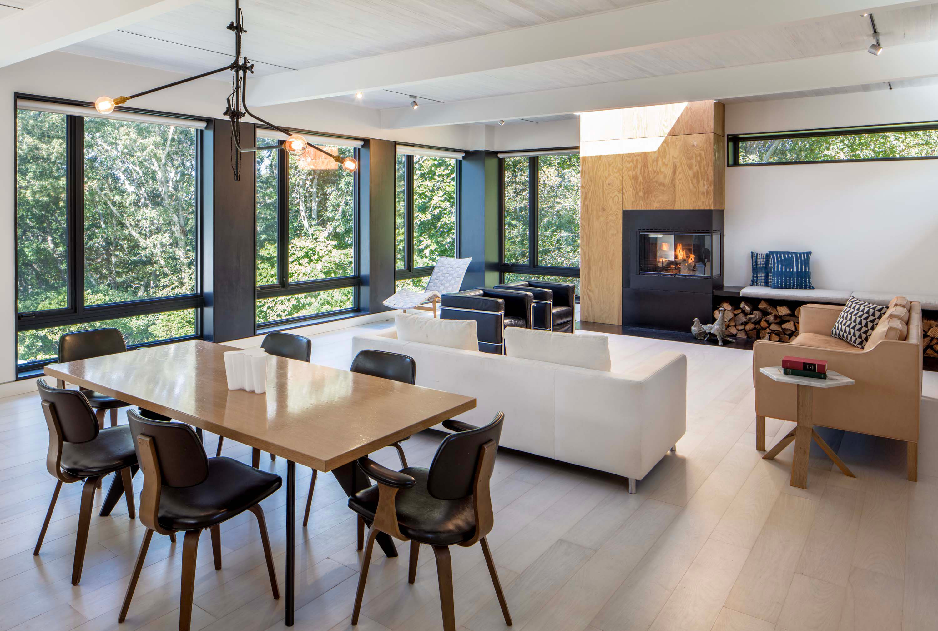 Living room of Bridgehampton House by Specht Novak Architects, featuring wood clad hearth and floor-to-ceiling windows. Shot by Taggart Sorensen.