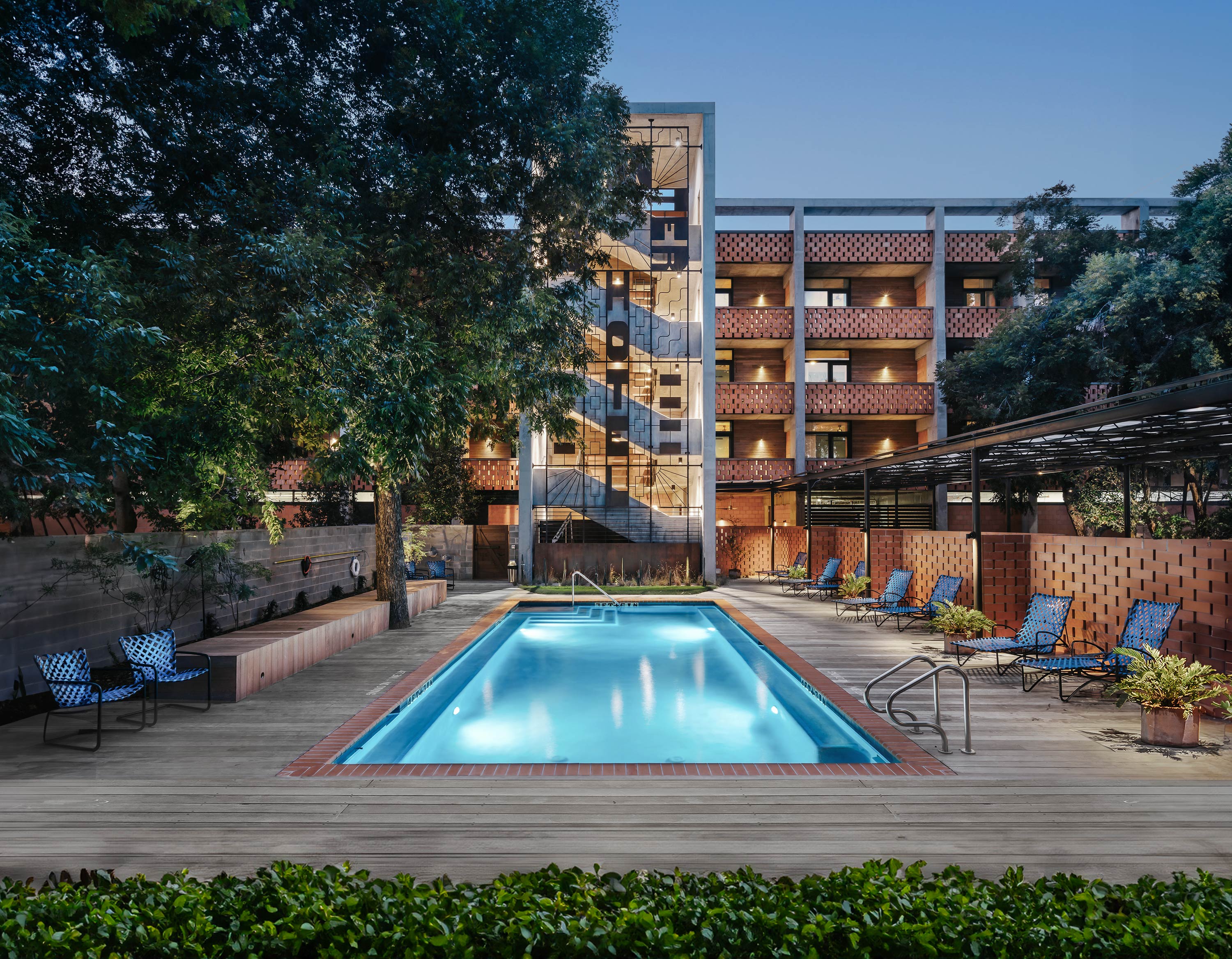 Exterior photo of the Carpenter Hotel by Specht Novak Architects. Shot by Chase Daniel, featuring the pool, lounging area surrounded by trees, and the hotel structure in the background.