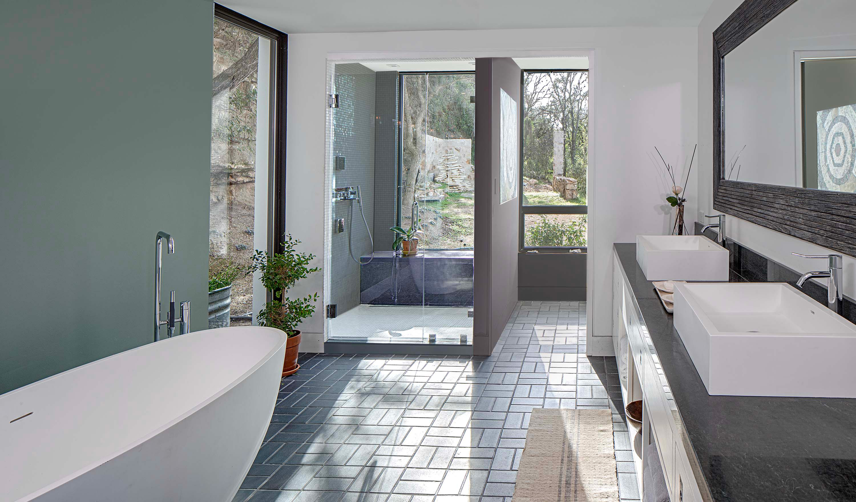 Interior photo of the Cliffside Residence by Specht Novak Architects. Shot by Andrea Calo, featuring a main bathroom, with bathtub, large shower, mosaic floors, and double vanity brightly illuminated by strategically placed glass walls.