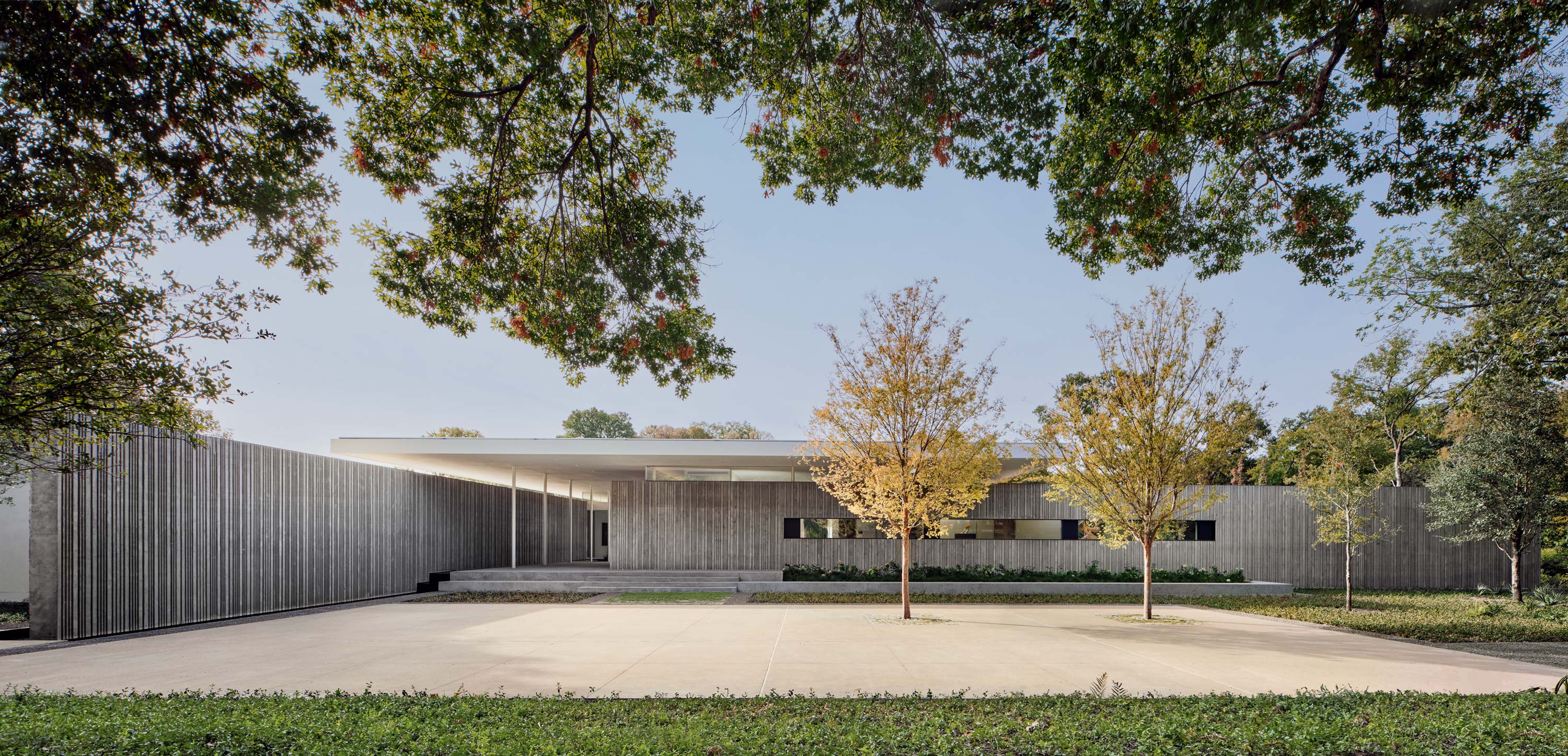 Exterior photo of the Preston Hollow Residence by Specht Novak Architects. Shot in the afternoon by Manolo Langis, featuring a concrete house and a vast green lawn.