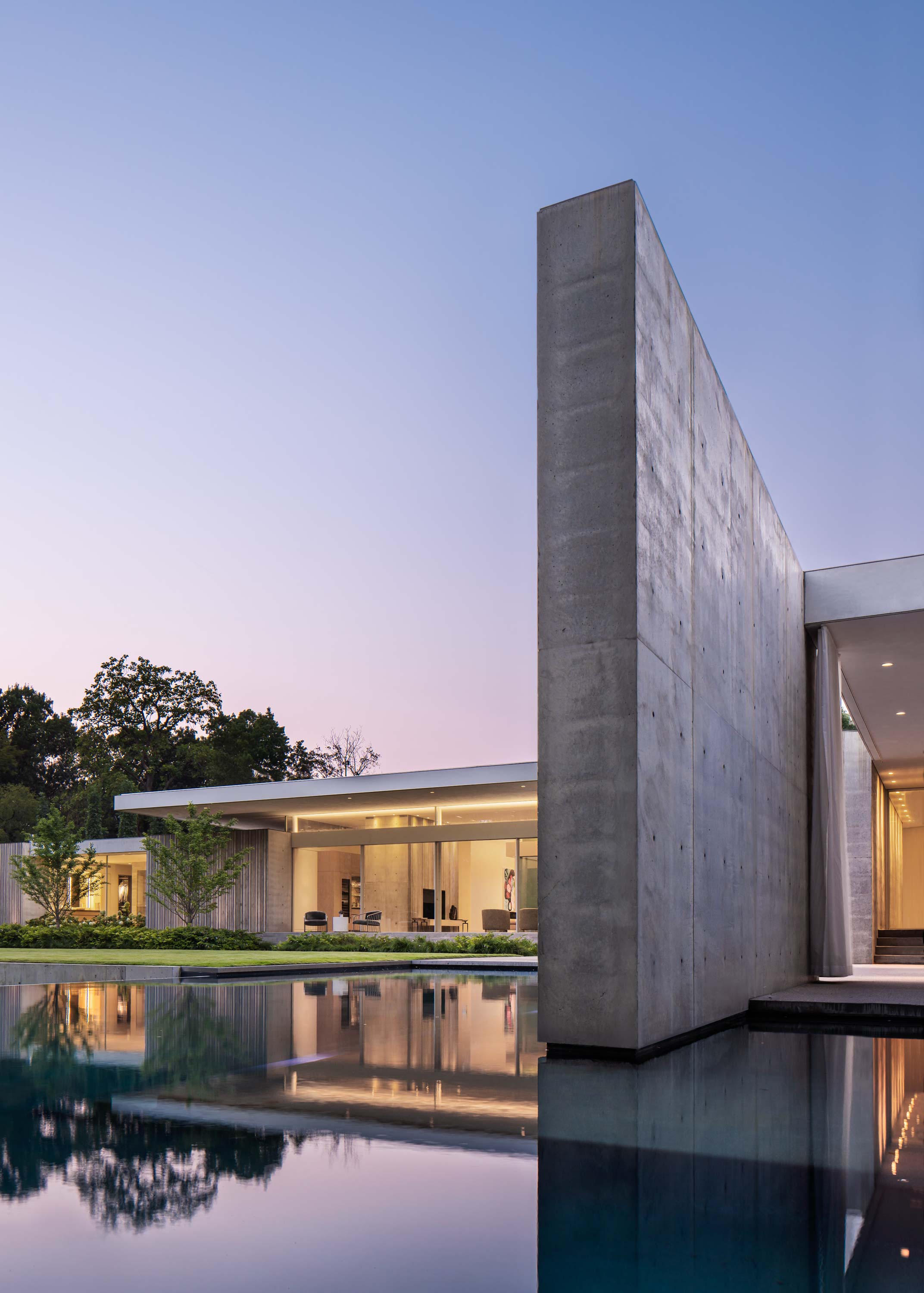Exterior photo of the Preston Hollow Residence by Specht Novak Architects. Shot at dusk by Manolo Langis, featuring pool, monolithic wall, and yard.
