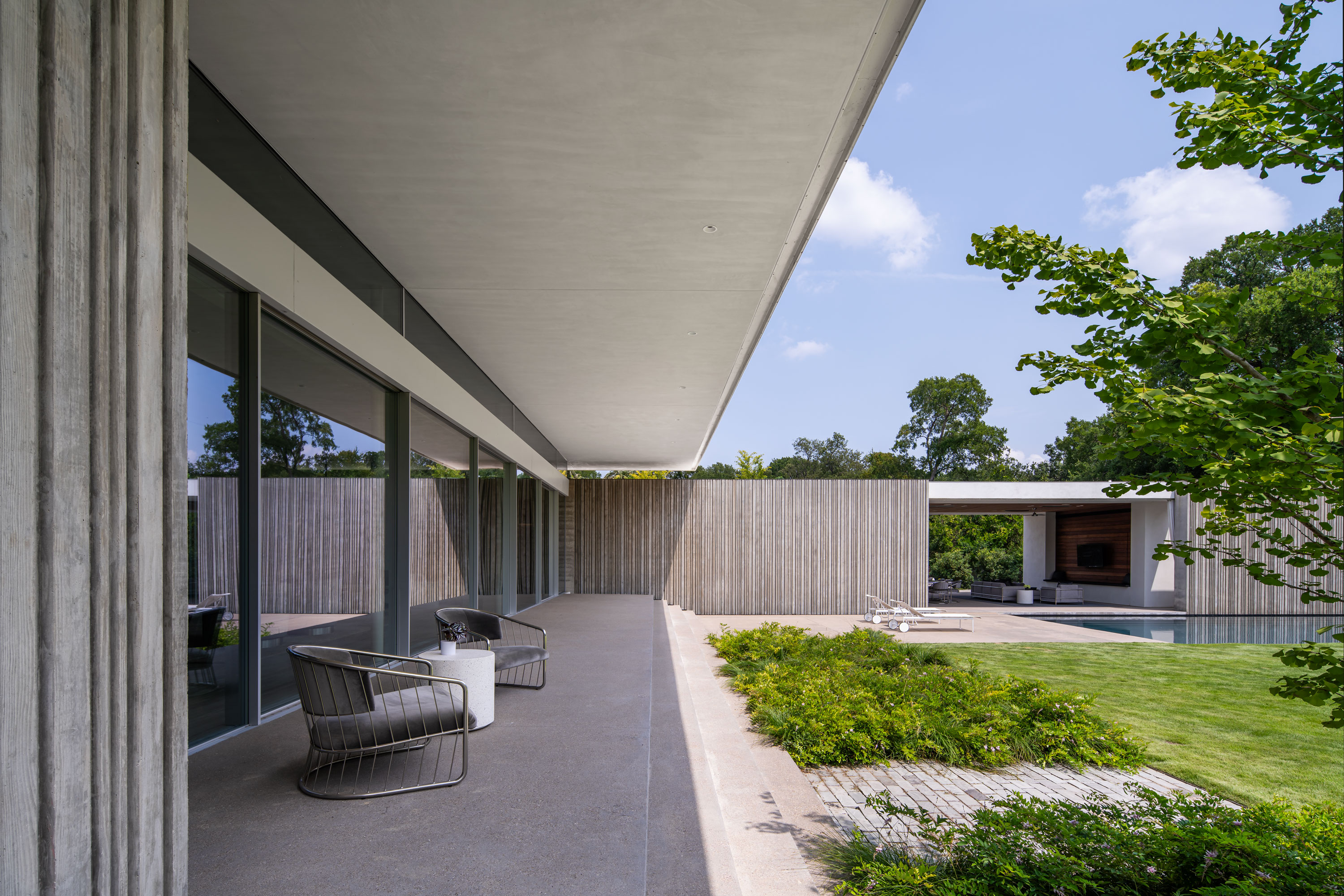 Exterior photo of the Preston Hollow Residence by Specht Novak Architects. Shot in the afternoon by Manolo Langis, featuring the living room terrace, pool, and rear lawn.