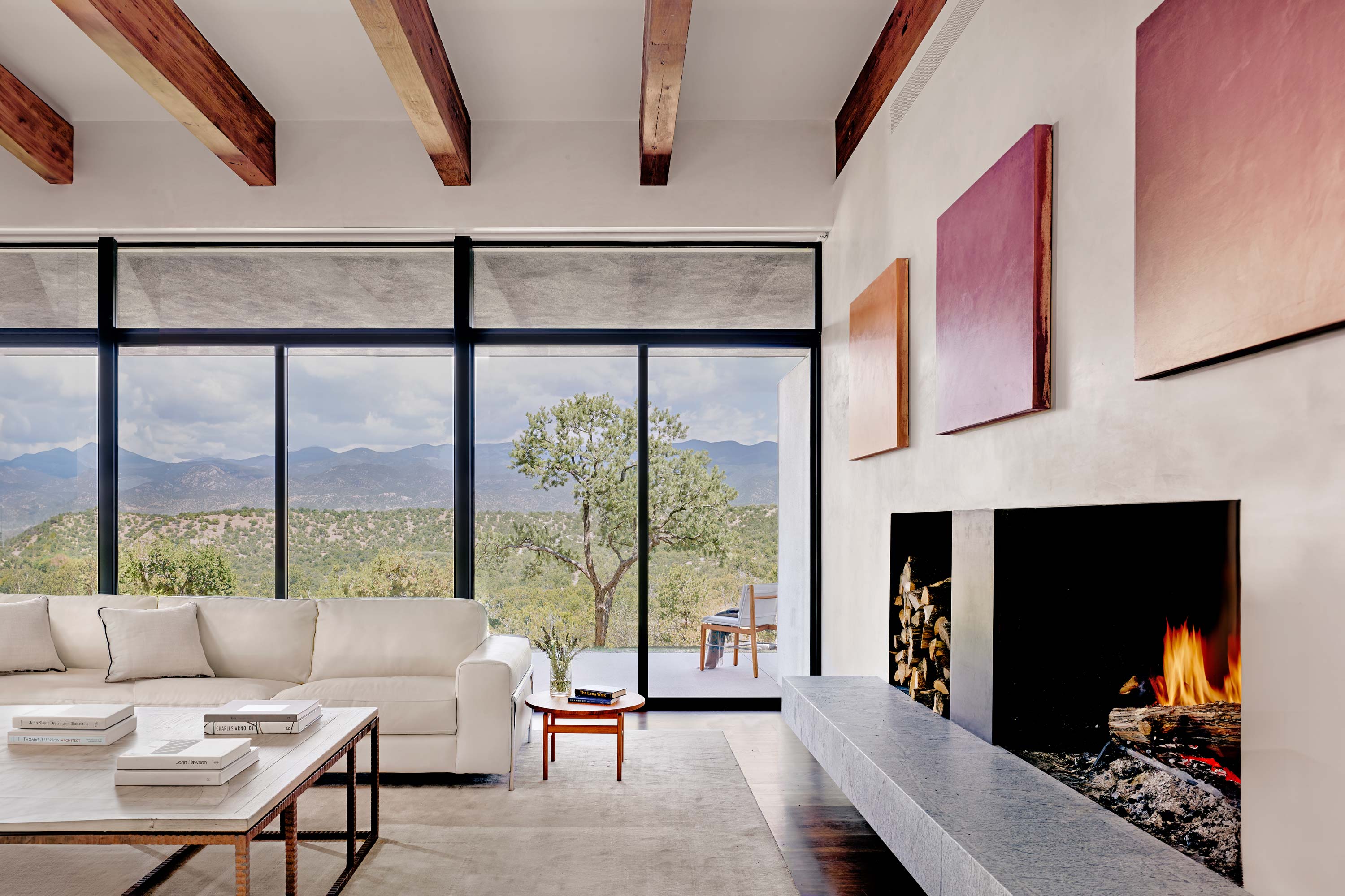 Interior photo of the Sangre de Cristo House by Specht Novak Architects. Shot by Casey Dunn, featuring a bright living area with beamed ceilings, Fireplace, and glass wall with views of mountains in the background.