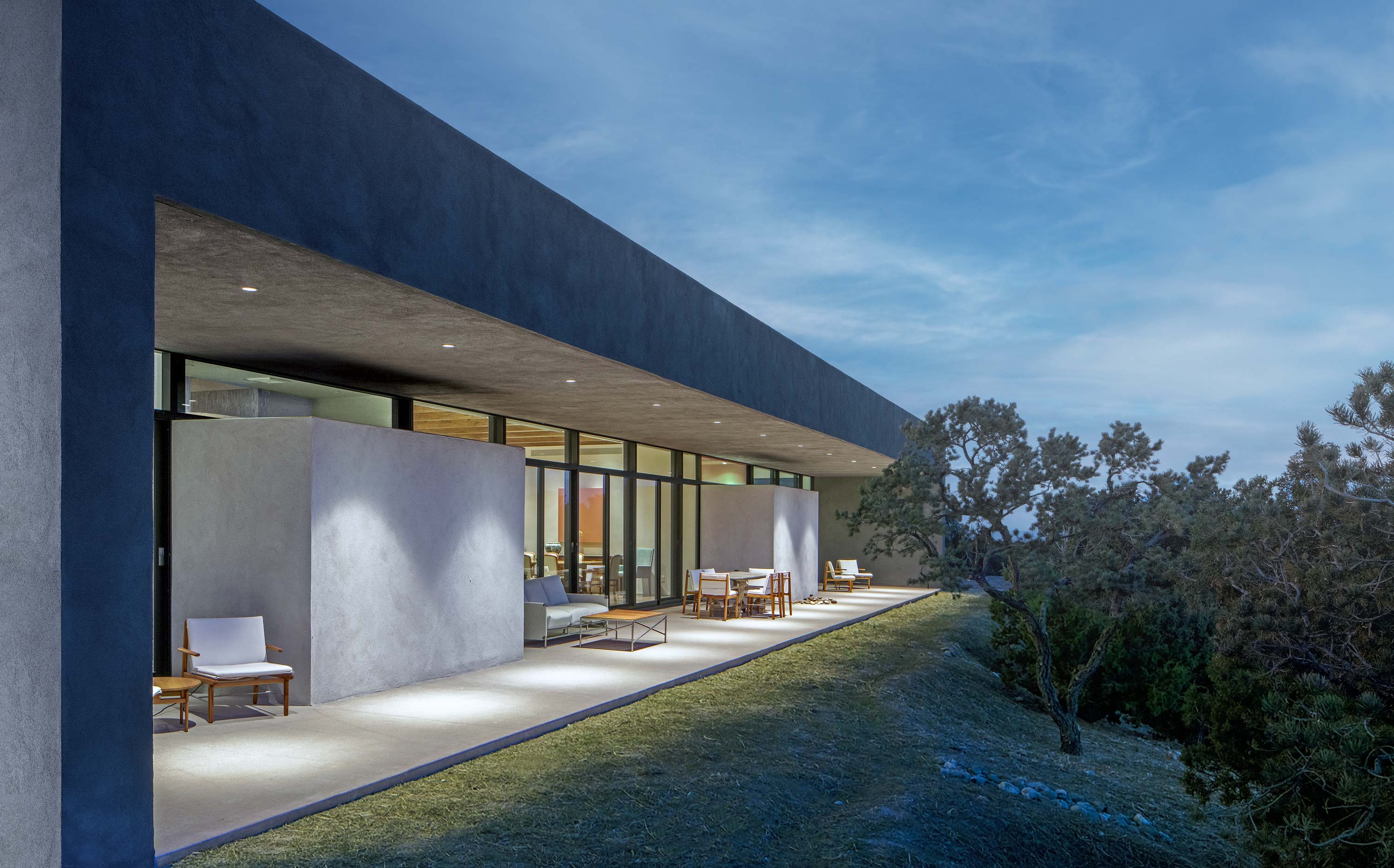 Exterior photo of the Sangre de Cristo House by Specht Novak Architects. Shot at dusk by Casey Dunn, featuring a covered deck on the perimeter of the house that faces its surrounding greenery.
