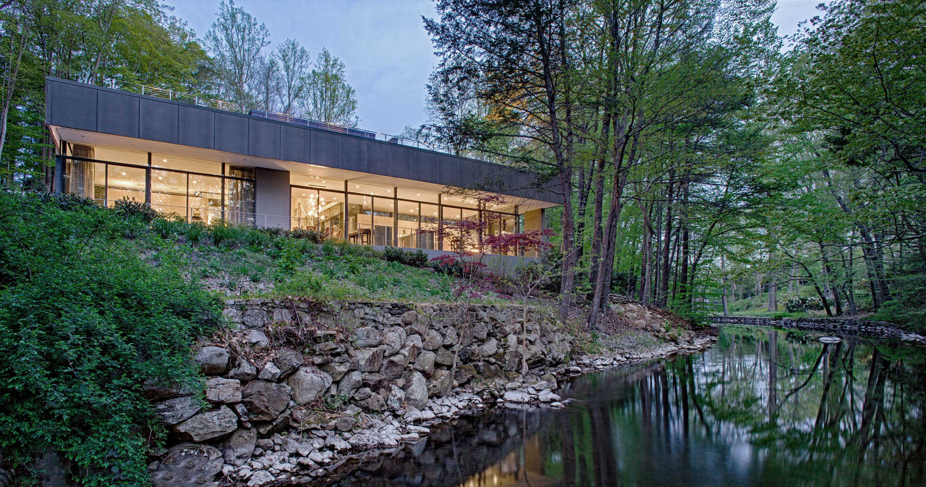 Exterior photo of Weston Residence by Specht Novak Architects. Shot by Jasper Lazor, featuring the concrete and glass home with roof gardens, and organic relation to its surrounding creek.