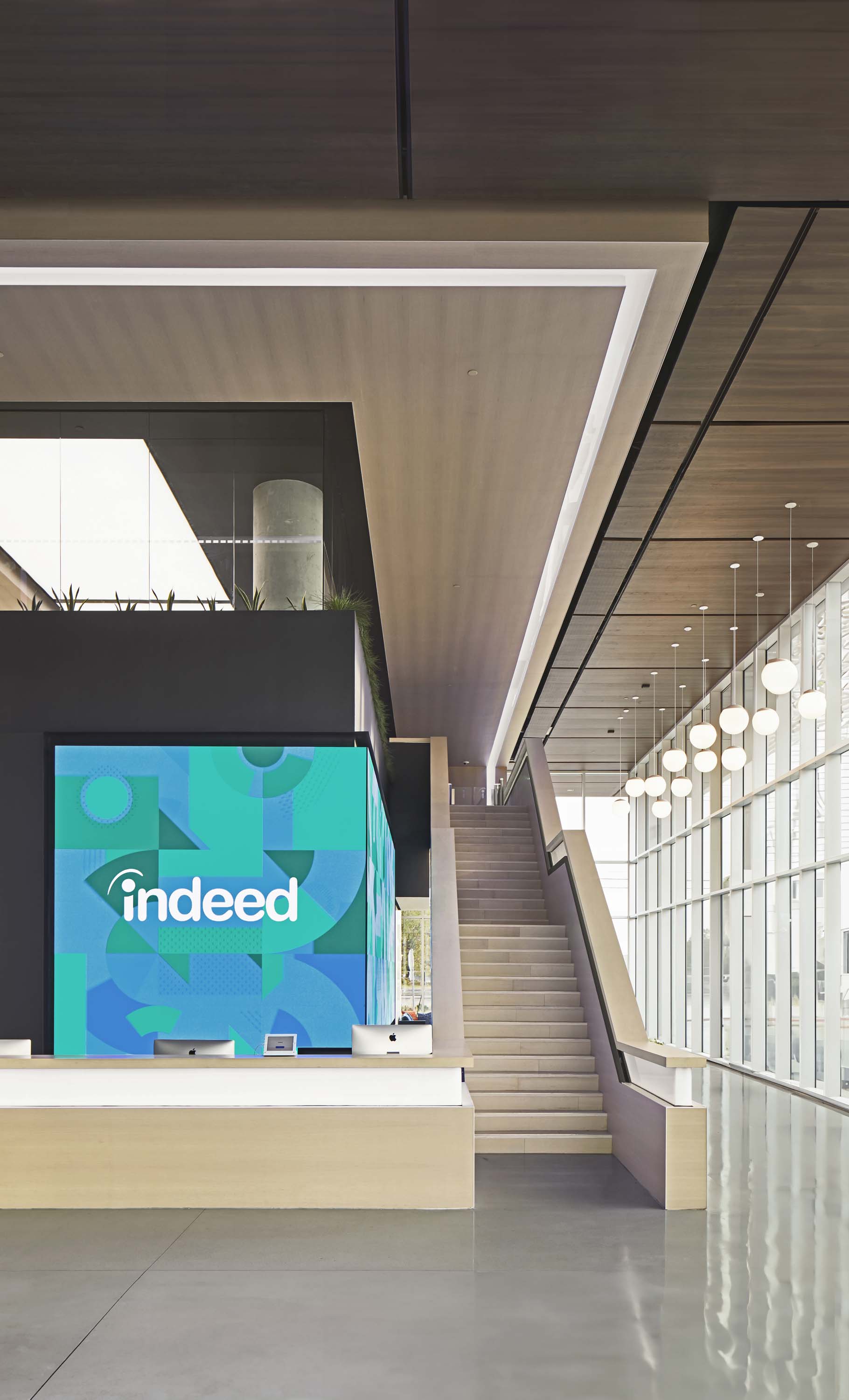 Indeed.com in Austin, Texas by Specht Novak Architects, shot by Andrea Calo, framed by desk and staircase showcasing cool toned materials and open floorplan.