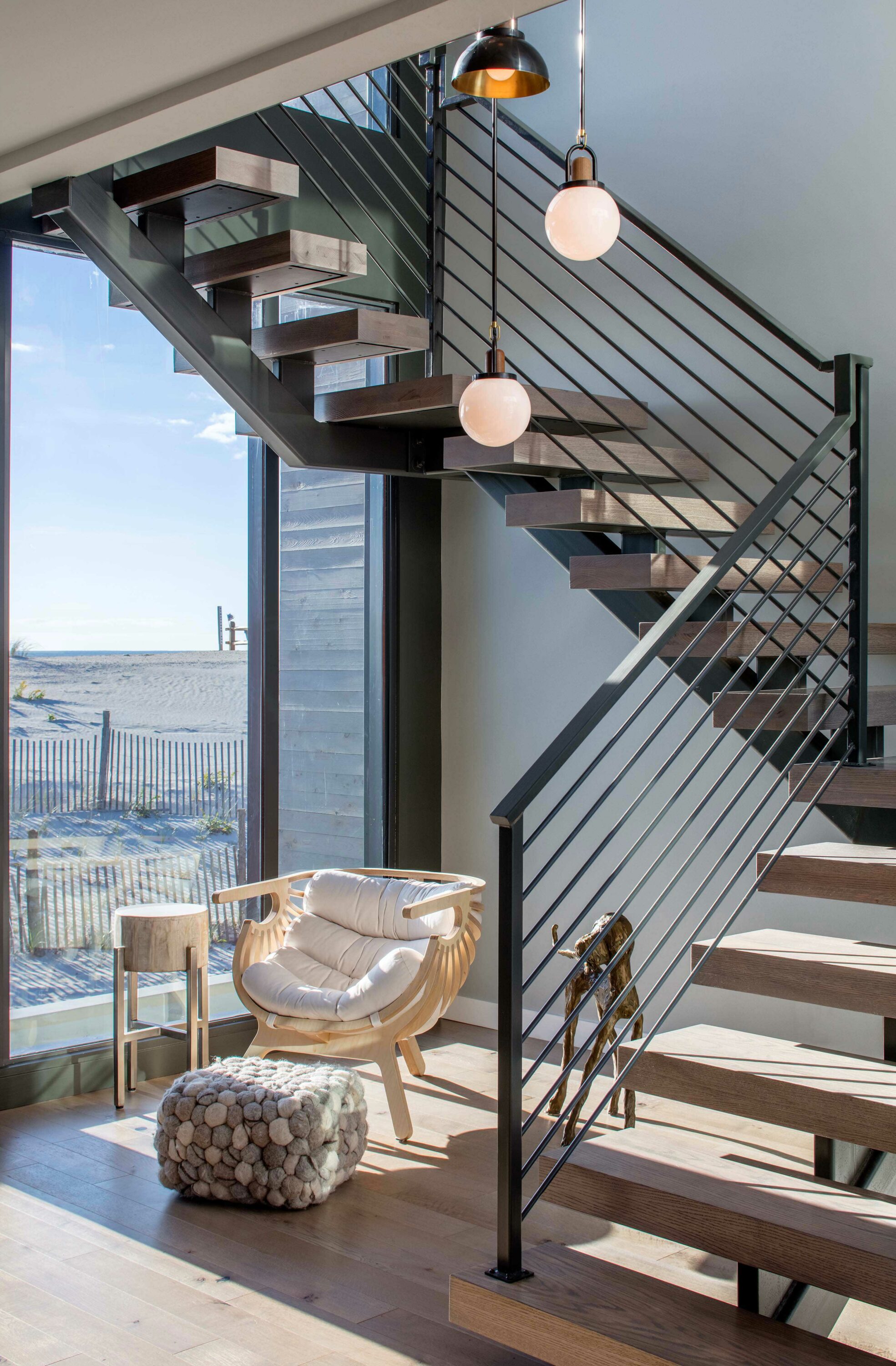 Interior photo of the Beach Haven Residence by Specht Novak Architects. Shot by Taggart Sorenson featuring brightly illuminated stairs with lounging area below them and a glass wall with views of the beach.