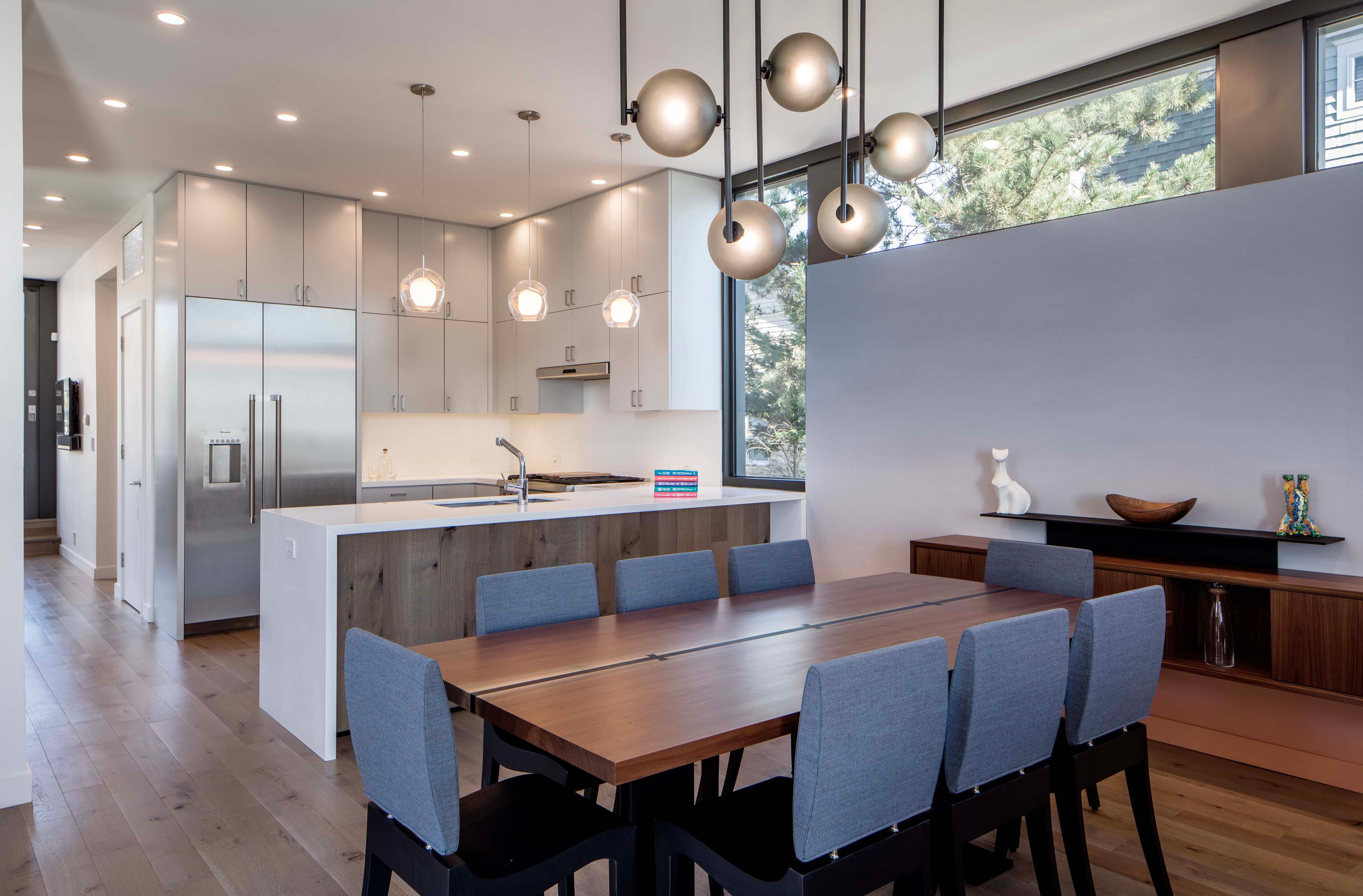 Interior photo of the Beach Haven Residence by Specht Novak Architects. Shot by Taggart Sorenson featuring dining room, island kitchen, and spherical lighting fixtures hanging from a tall ceiling.