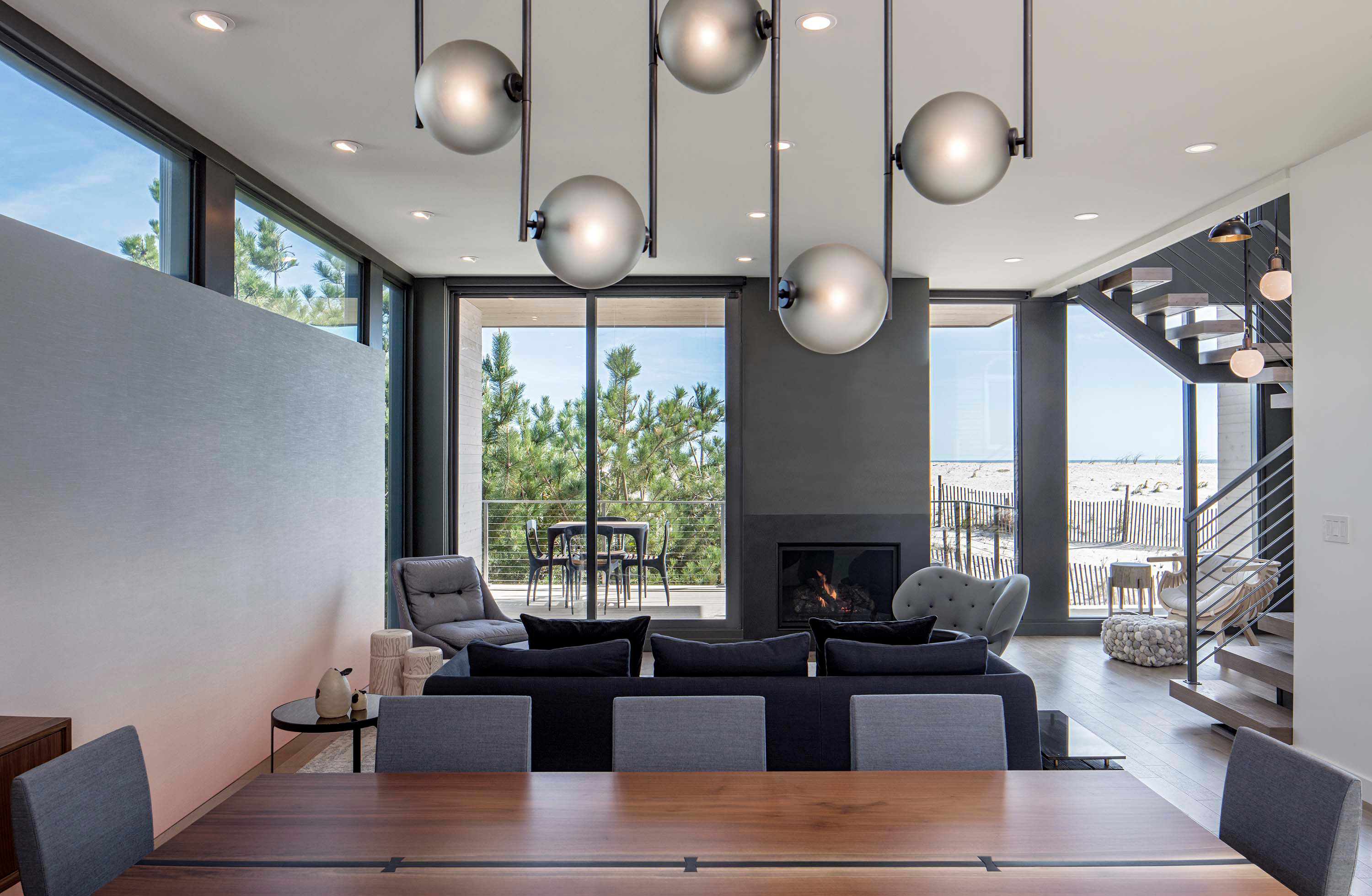 Interior photo of the Beach Haven Residence by Specht Novak Architects. Shot by Taggart Sorenson featuring a spacious dining area, lounging area with fireplace, and the beach in the background.