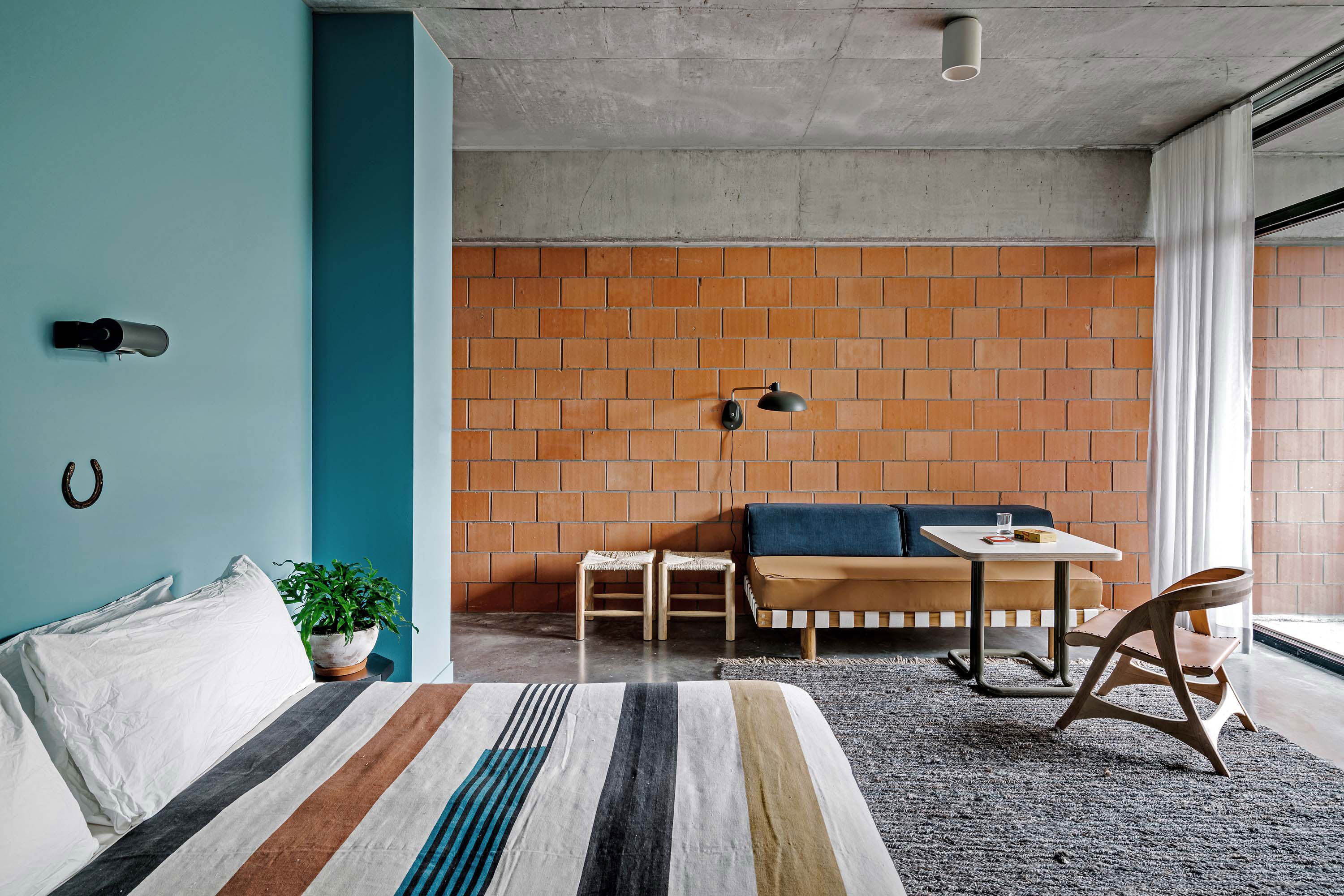 Interior photo of the Carpenter Hotel by Specht Novak Architects. Shot by Chase Daniel, featuring a room with brick walls, bed, and lounging area in neutral and blue tones.