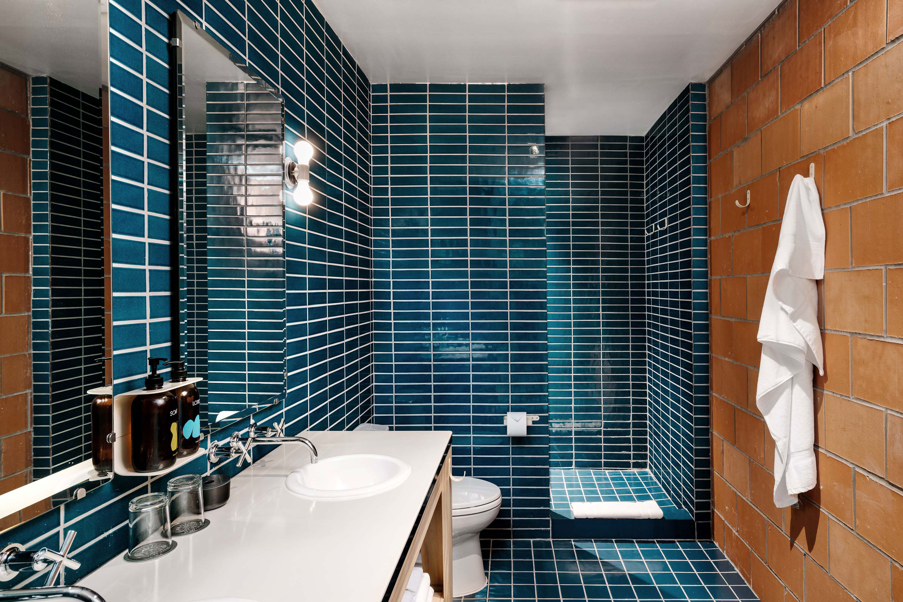Interior photo of the Carpenter Hotel by Specht Novak Architects. Shot by Chase Daniel, featuring a large bathroom vanity with rich blue tiles and brick accent wall.