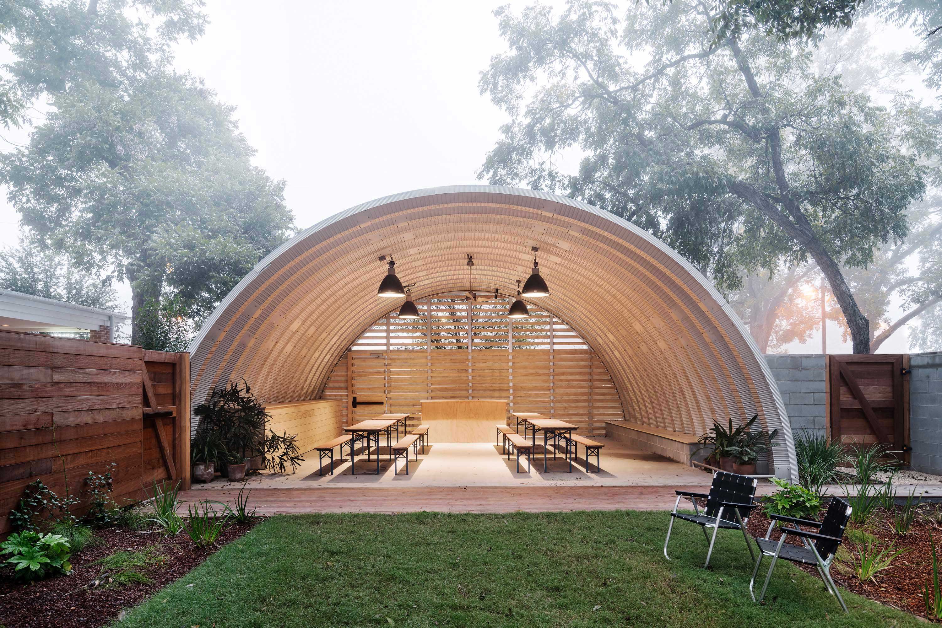 Interior photo of the Carpenter Hotel by Specht Novak Architects. Shot by Chase Daniel, featuring a barnlike arch structure over a communal sitting area adjacent to a yard, surrounded by trees.