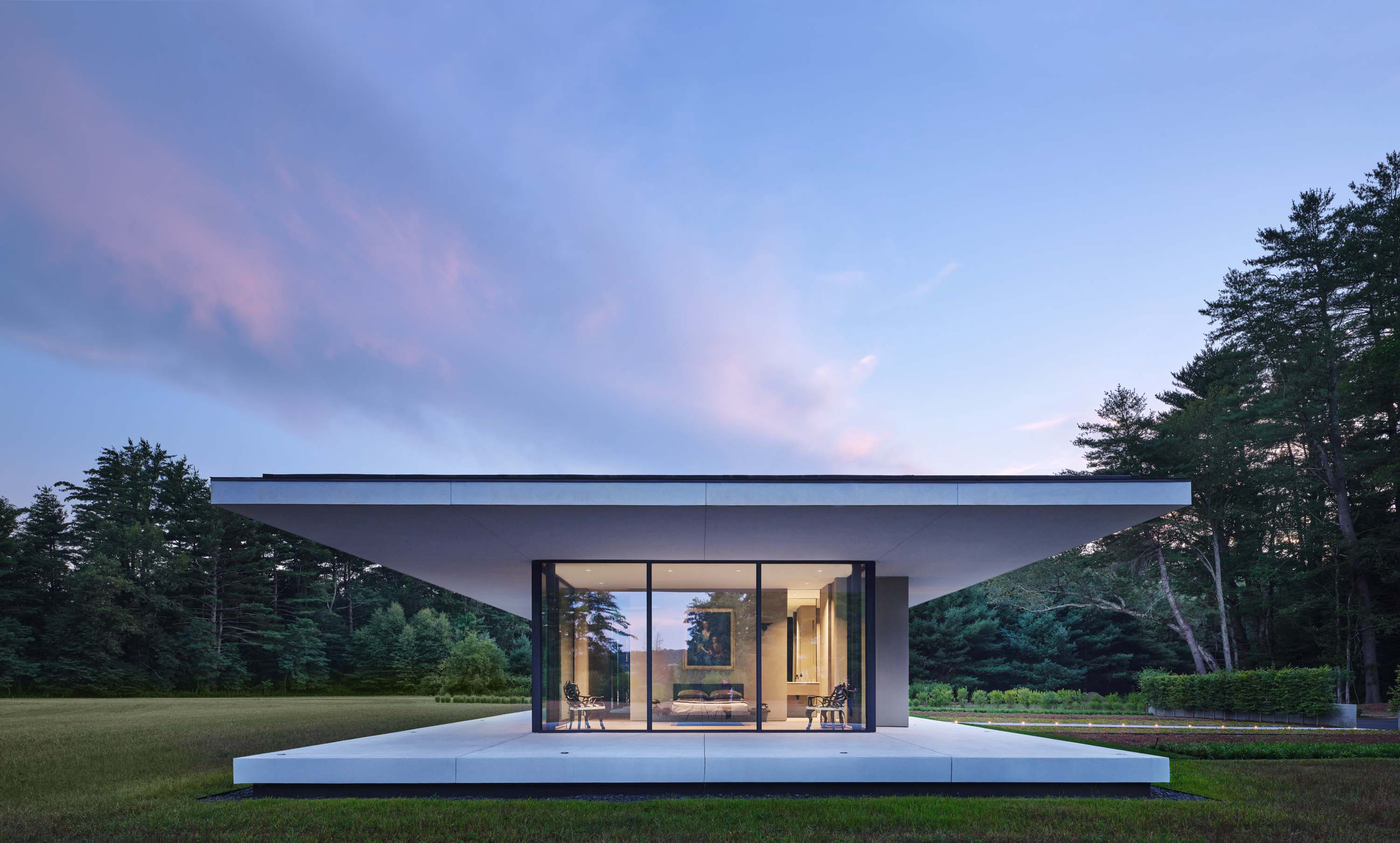 Exterior photo of the Casa Annunziata Residence by Specht Novak Architects. Shot at dusk by Dror Baldinger, featuring a side view of the symmetrical single-story pavilion with a thin floating roof that cantilevers 15’ from the perimeter walls, in perfect harmony with its natural surroundings.