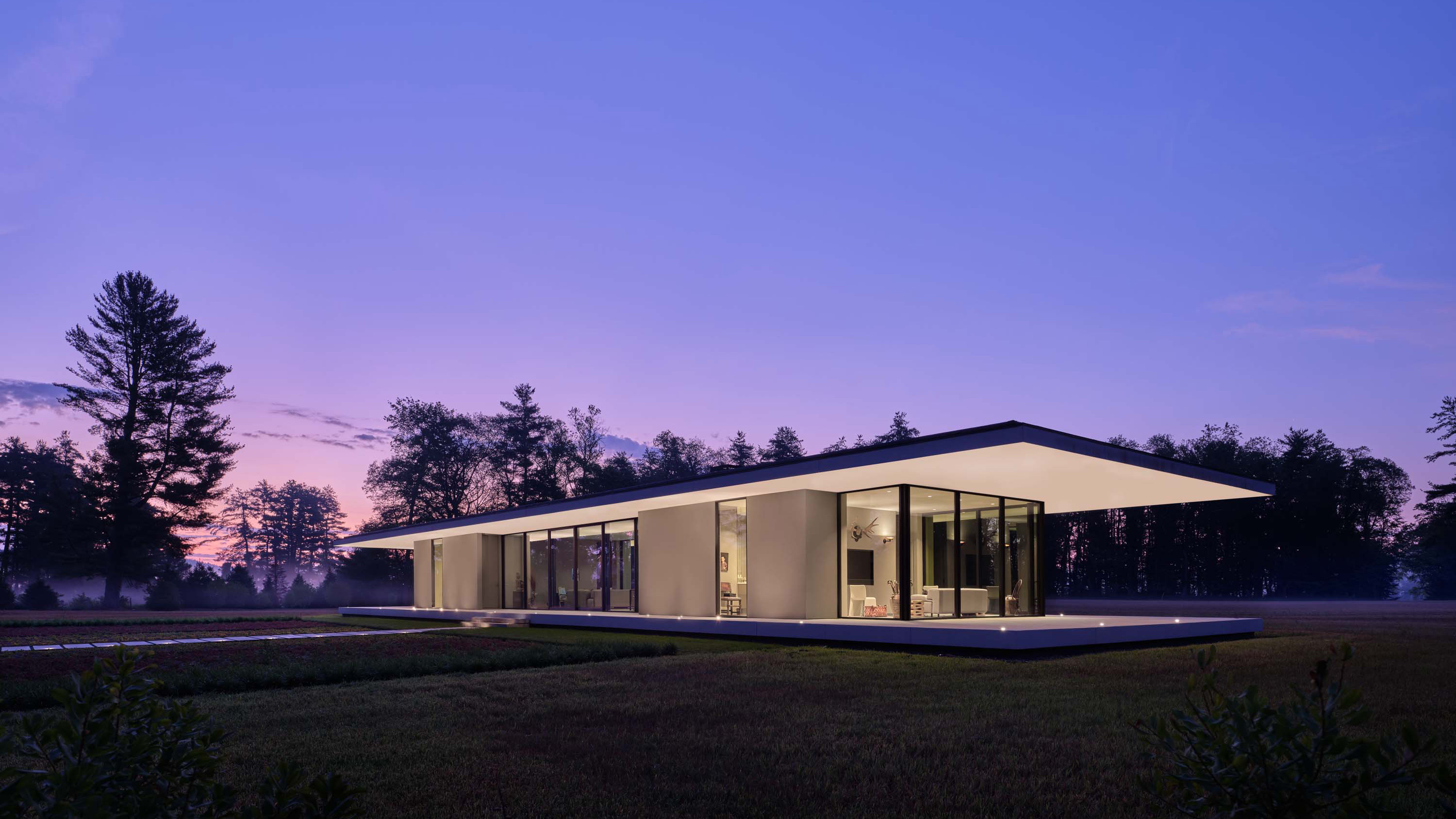 Exterior photo of the Casa Annunziata Residence by Specht Novak Architects. Shot at dusk by Dror Baldinger, featuring a Diagonal view of the symmetrical single-story pavilion with a thin floating roof that cantilevers 15’ from the perimeter walls, in perfect harmony with its natural surroundings.
