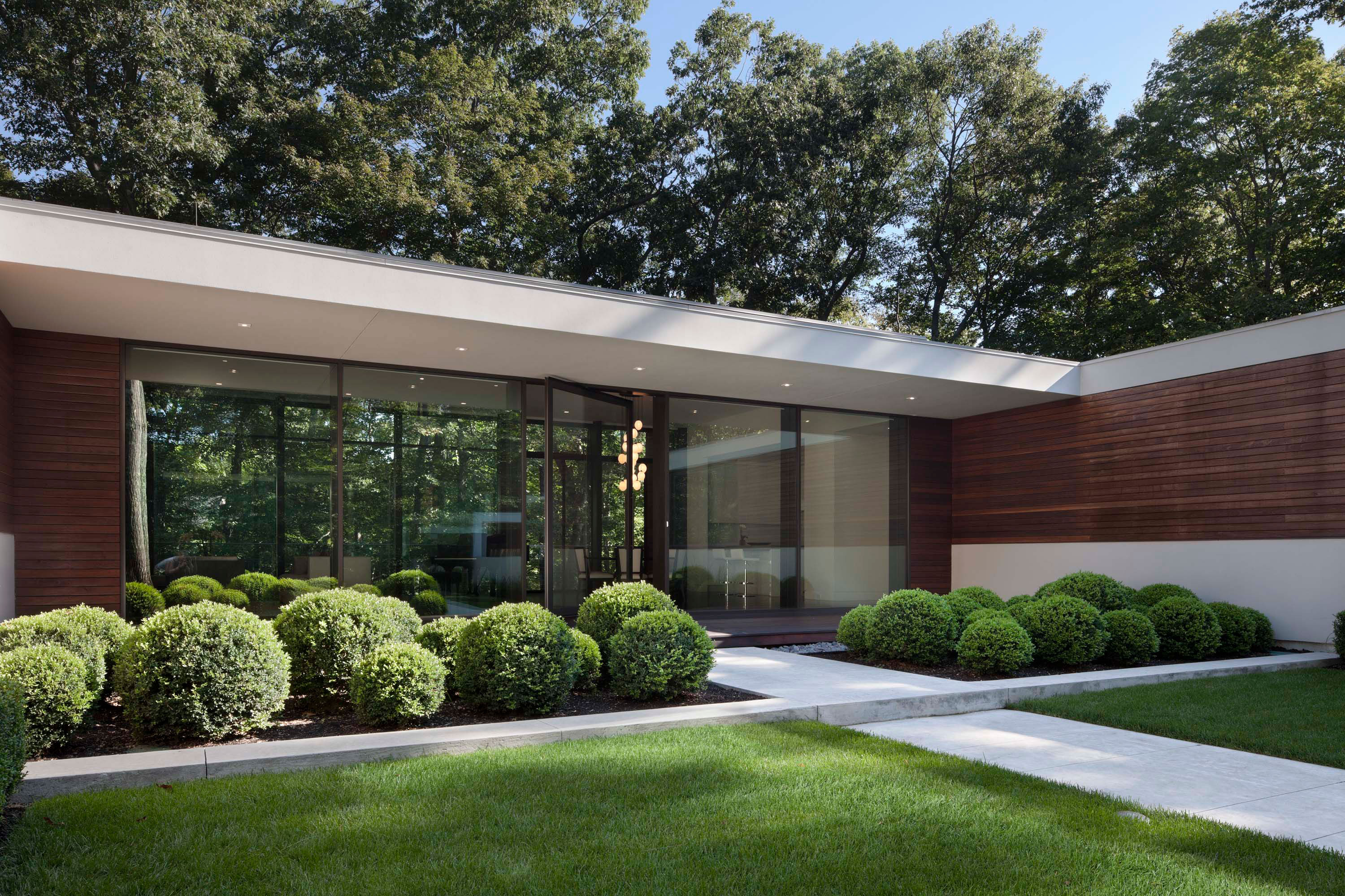 Exterior photo of the New Canaan Residence by Specht Novak Architects. Shot by Elizabeth Felicella featuring the glass and concrete structure from a side view of the home highlighting a connecting garden.