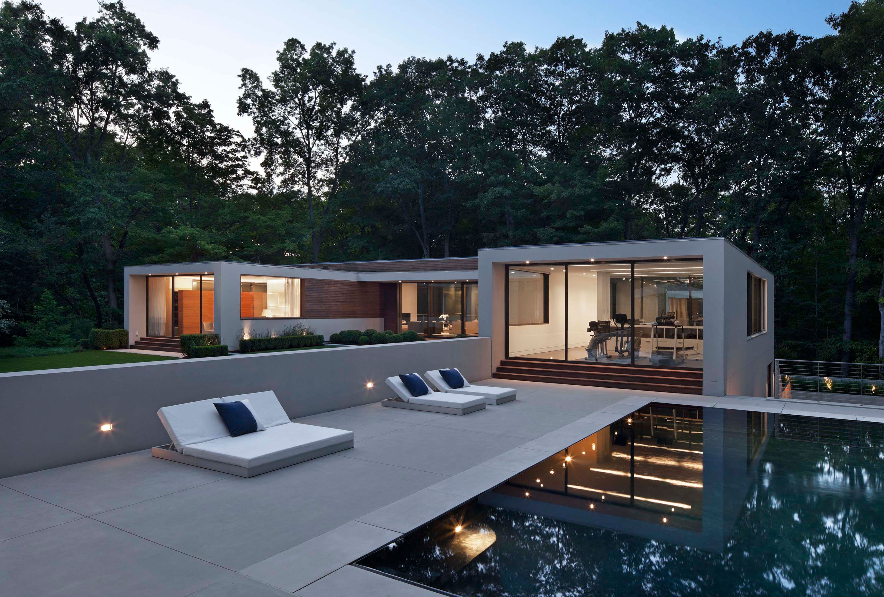 Exterior photo of the New Canaan Residence by Specht Novak Architects. Shot by Elizabeth Felicella featuring the symmetrical home, pool, and lounging area embraced by trees.