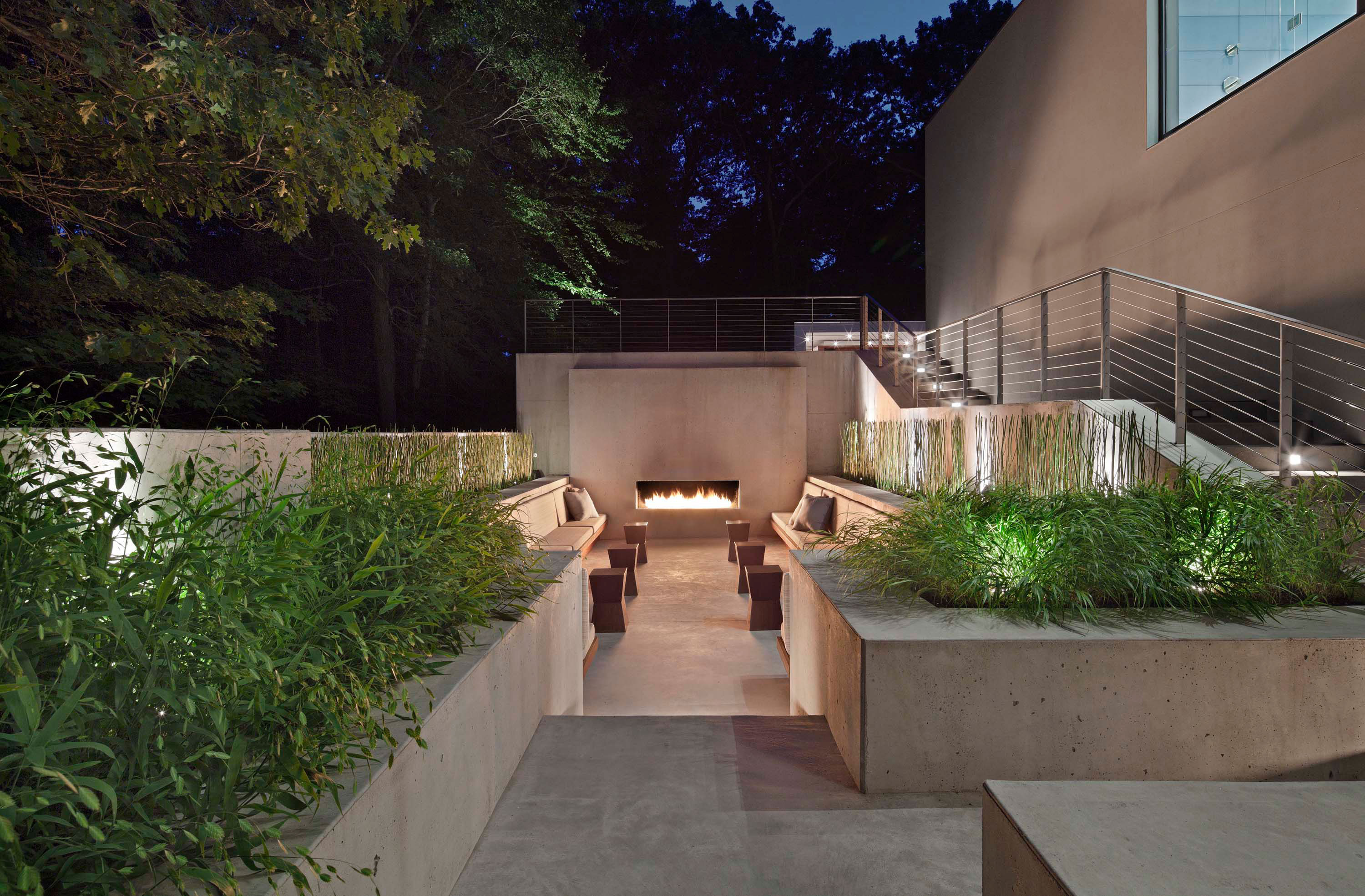 Exterior photo of the New Canaan Residence by Specht Novak Architects. Shot by Elizabeth Felicella featuring a fireplace and lower level lounge area embraced by the trees and surrounding greenery.
