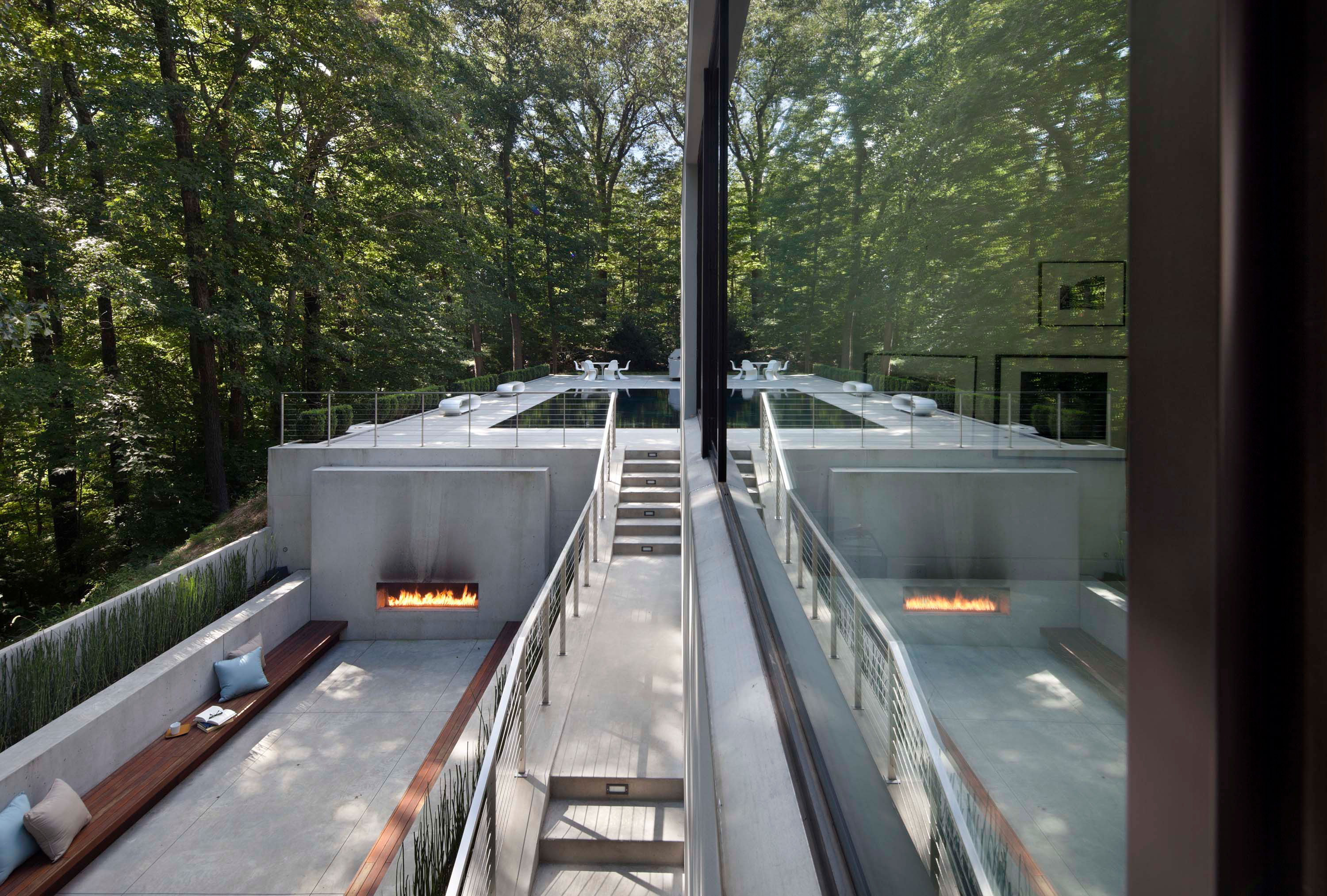 Exterior photo of the New Canaan Residence by Specht Novak Architects. Shot from upper level by Elizabeth Felicella, featuring a fireplace and lower level lounge area embraced by the trees and surrounding greenery.