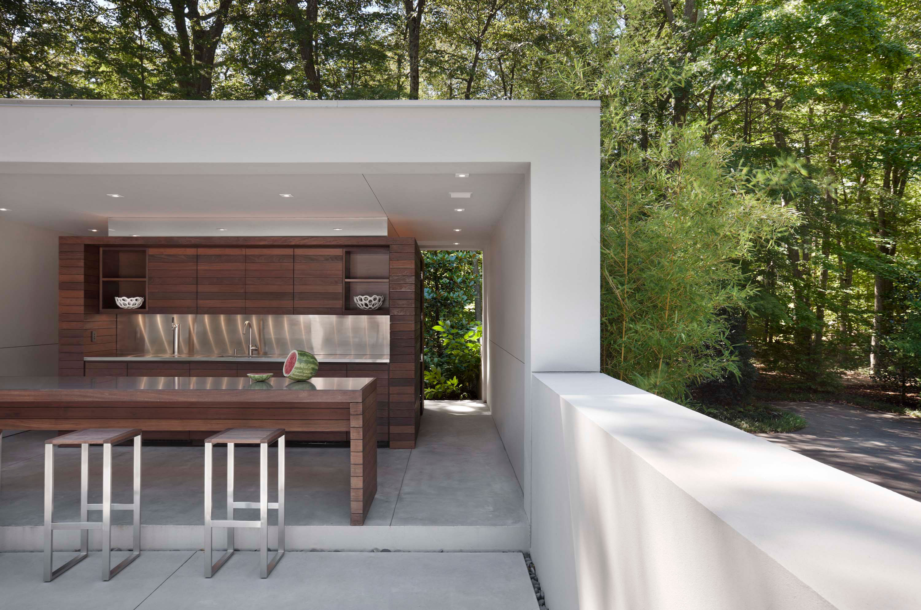 Exterior photo of the New Canaan Residence by Specht Novak Architects. Shot by Elizabeth Felicella featuring dining/bar area by the pool, surrounded by trees.