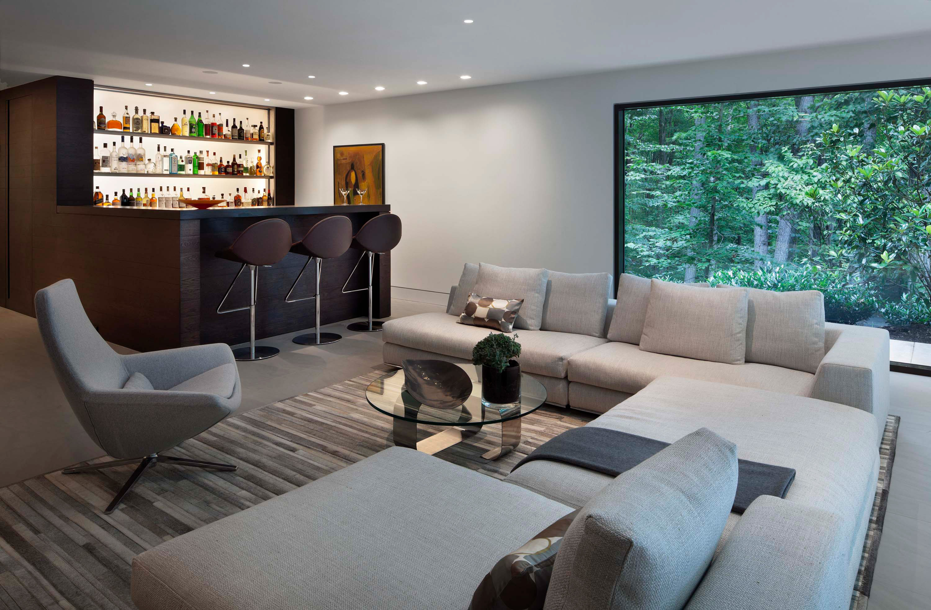 Interior photo of the New Canaan Residence by Specht Novak Architects. Shot by Elizabeth Felicella featuring a mini bar and adjacent lounging area with a large sectional couch, complementing chair, and glass wall.