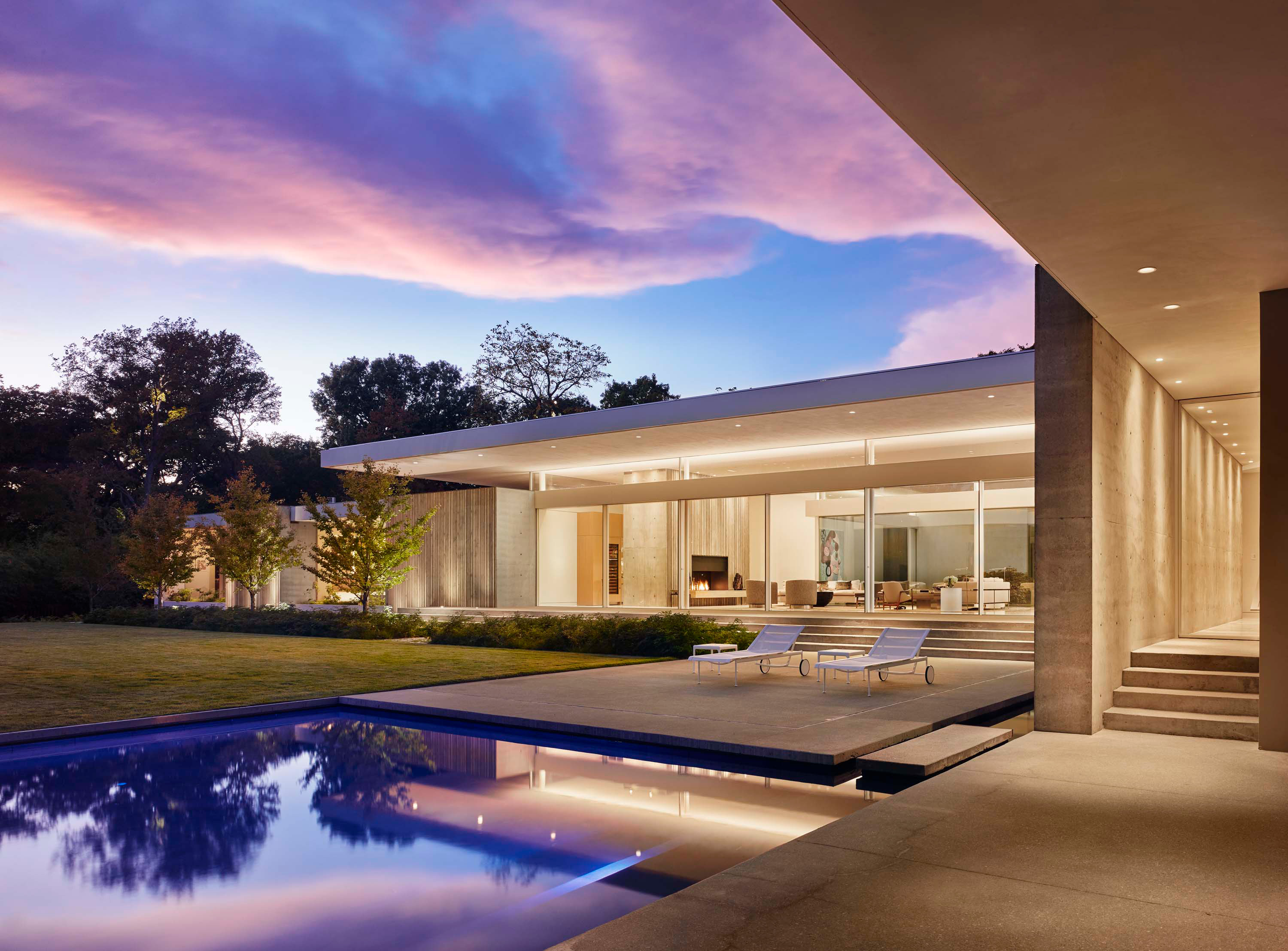 Exterior photo of the Preston Hollow Residence by Specht Novak Architects. Shot at dusk by Manolo Langis, featuring an entry hallway, the pool, yard, lounging areas, and glowing home.