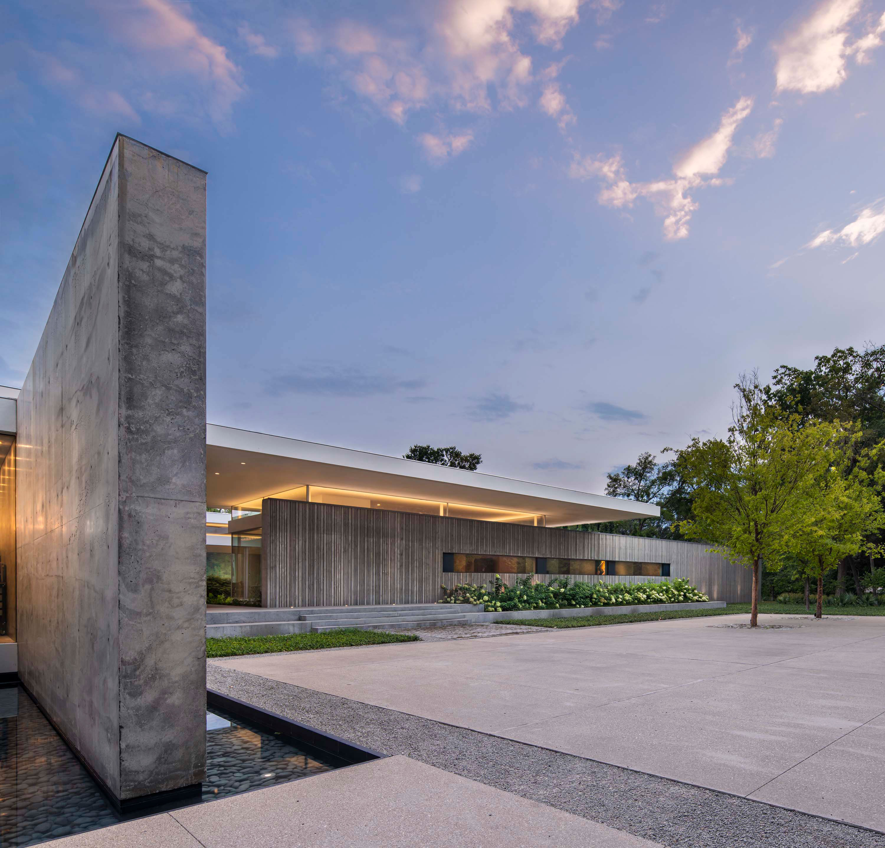 Exterior photo of the Preston Hollow Residence by Specht Novak Architects. Shot at dusk by Manolo Langis, featuring the glowing home, and monolithic concrete wall.
