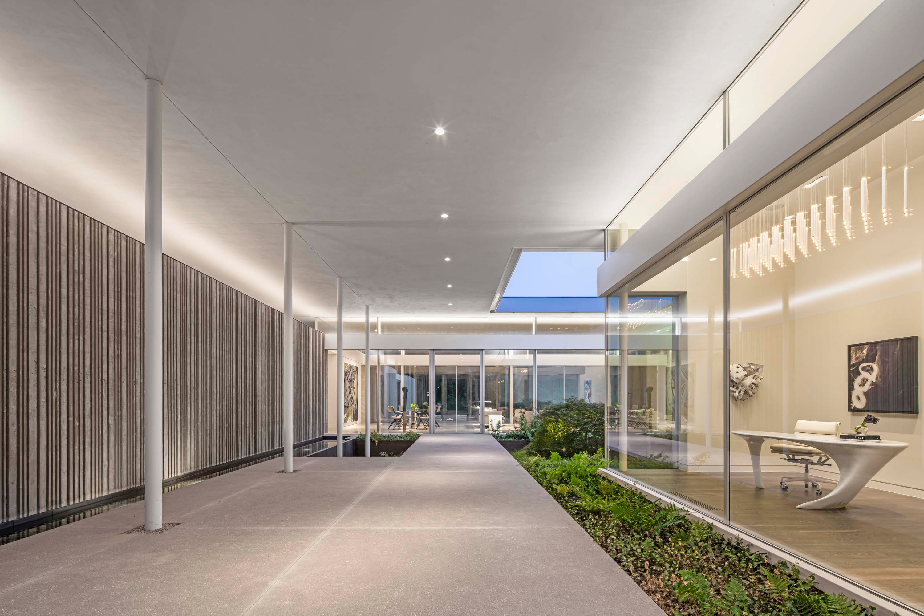Hallway photo of the Preston Hollow Residence by Specht Novak Architects. Shot by Manolo Langis, featuring a welcoming hallway with a row of columns, greenery, and office space.