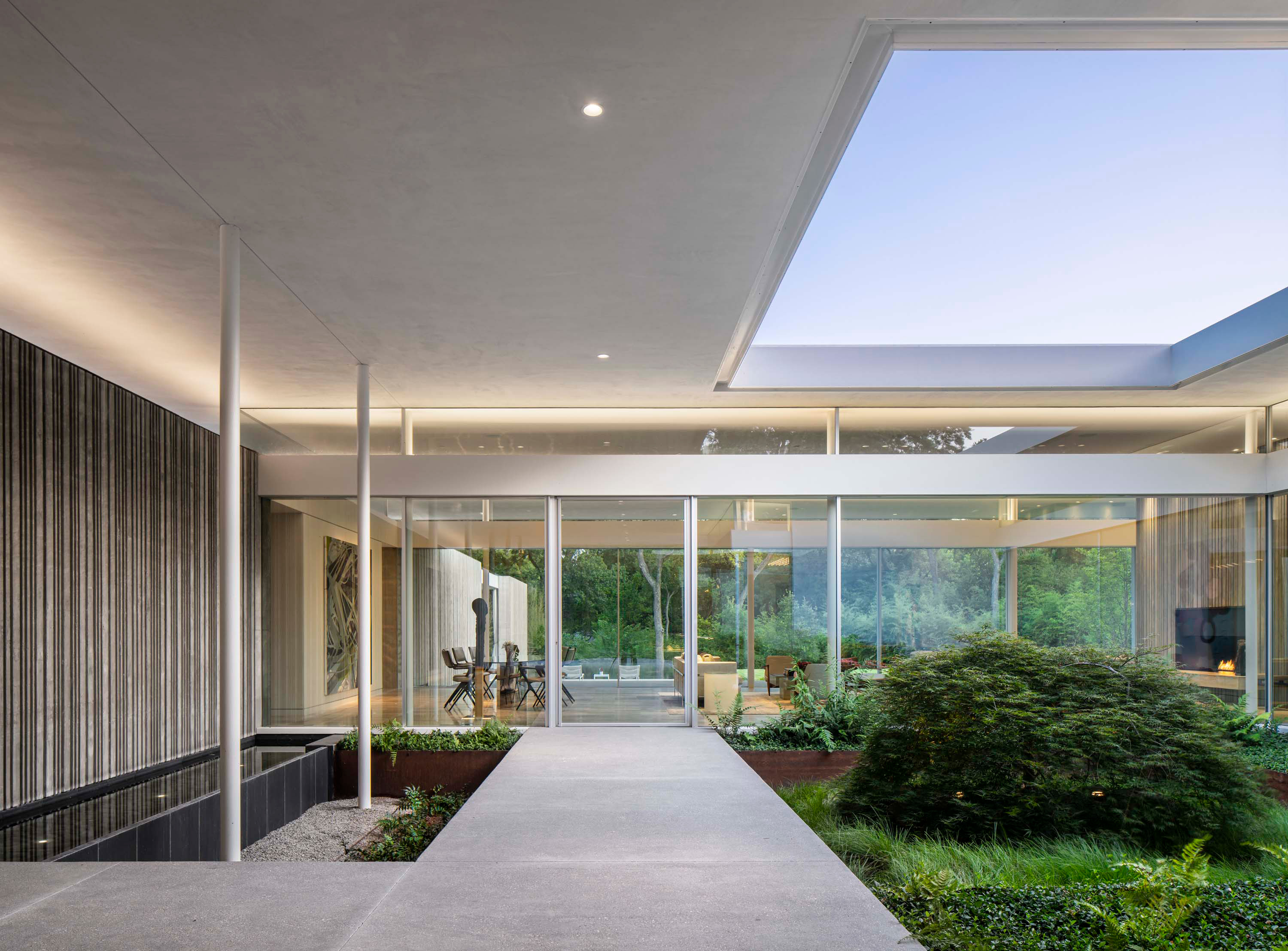 Interior photo of the Preston Hollow Residence by Specht Novak Architects. Shot in the afternoon by Manolo Langis, featuring a hallway that leads to a living space with a water feature on its right and indoor garden with open roof to its right.