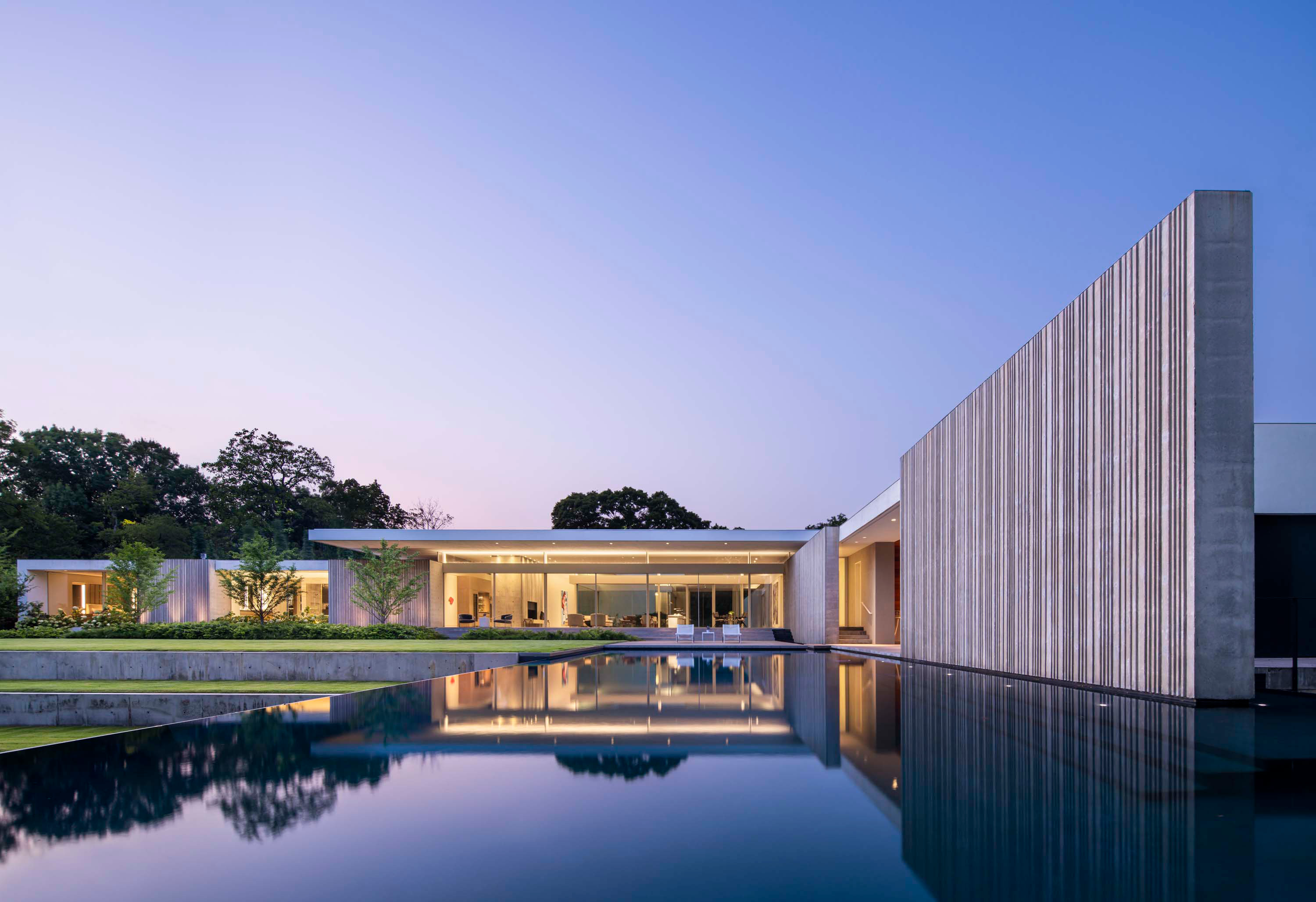 Exterior photo of the Preston Hollow Residence by Specht Novak Architects. Shot at dusk by Manolo Langis, featuring the pool, glowing home, and monolithic concrete wall.