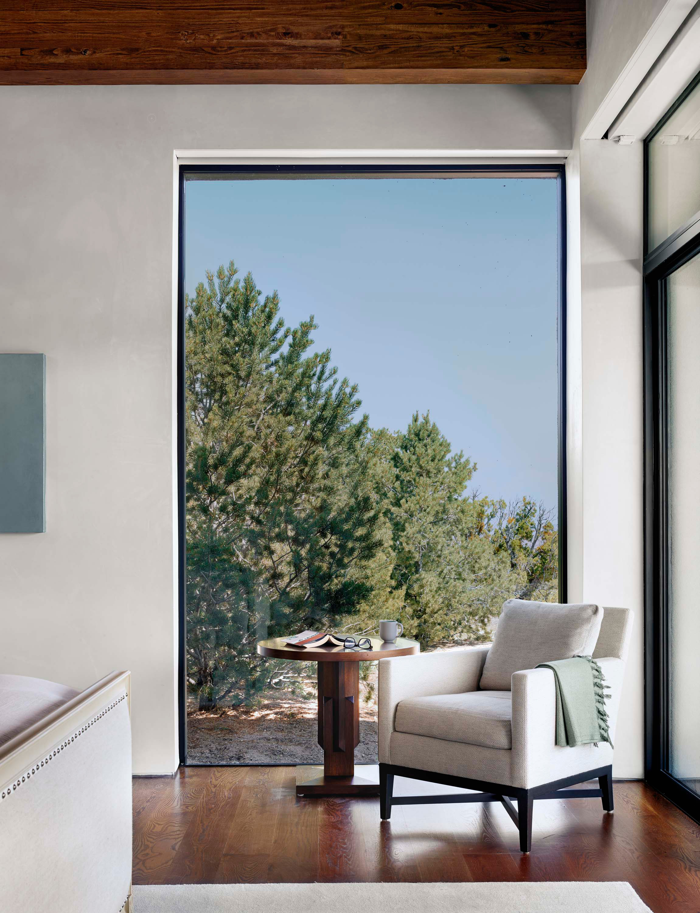 Interior photo of the Sangre de Cristo House by Specht Novak Architects. Shot by Casey Dunn, featuring a bright lounging area of a bedroom with a glass wall and views of surrounding greenery.