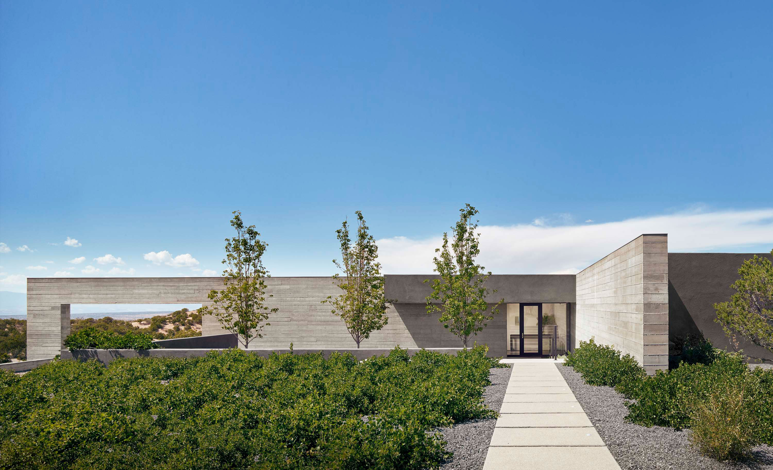 Exterior photo of the Sangre de Cristo House by Specht Novak Architects. Shot by Casey Dunn, featuring welcoming entryway surrounded by greenery and monolithic concrete wall.