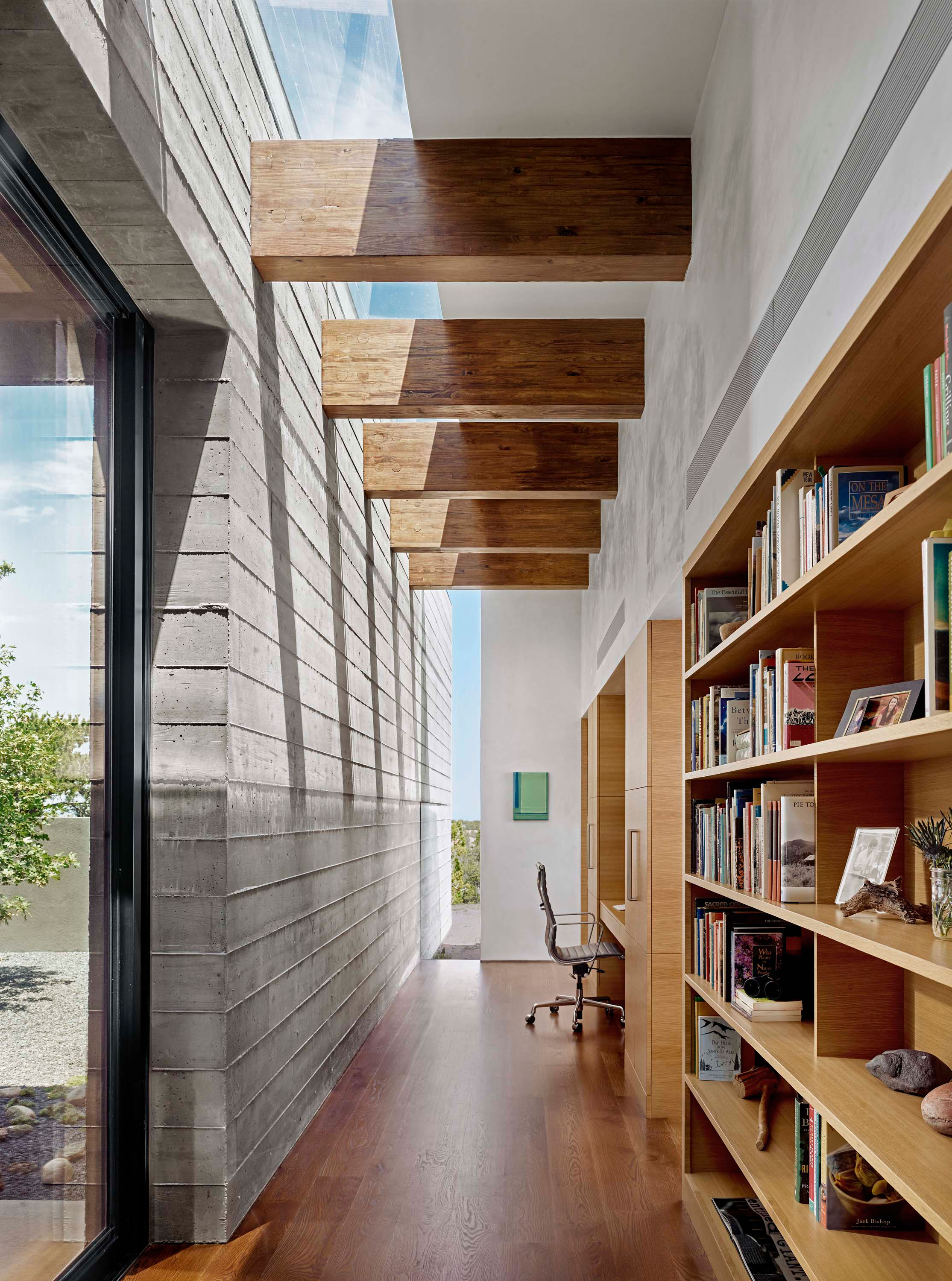Interior photo of the Sangre de Cristo House by Specht Novak Architects. Shot by Casey Dunn, featuring a bright office space, bookshelves, and beamed ceiling across a longitudinal hallway.