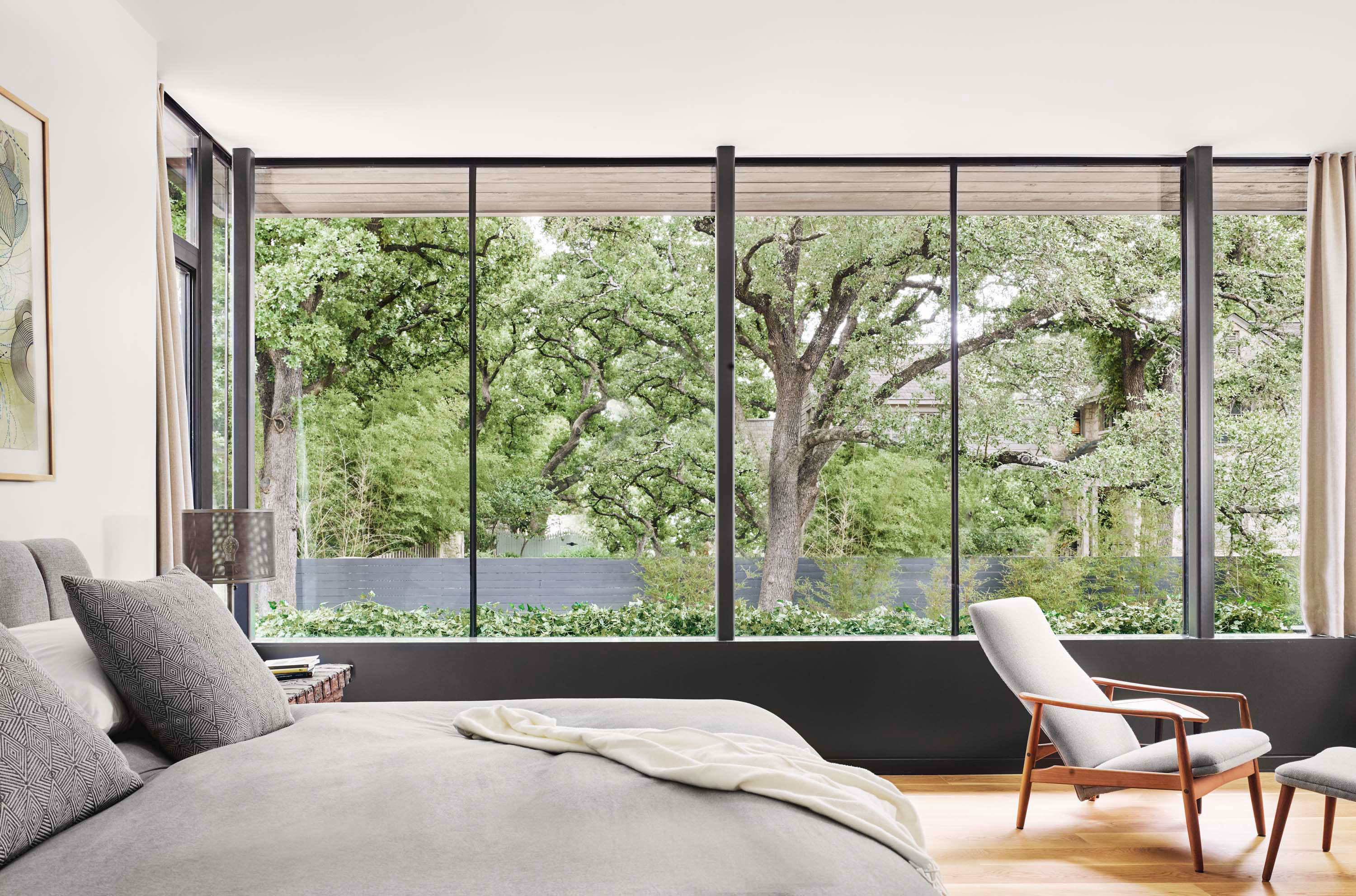 Interior photo of the Treetops House residence by Specht Novak Architects. Shot by Casey Dunn, featuring a bedroom with wooden floors, and frameless glass windows that showcase the natural surroundings of the home.