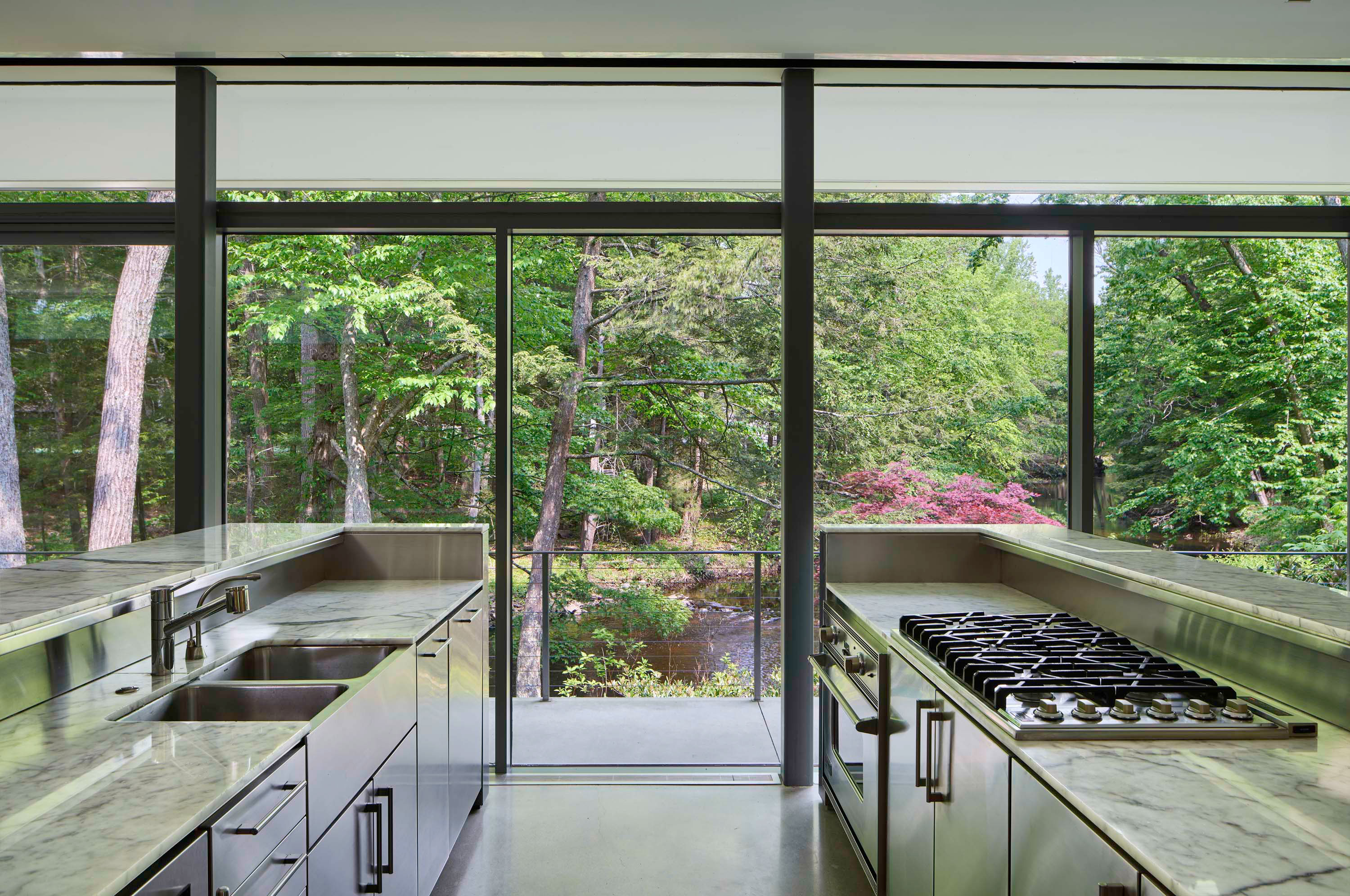 Interior photo of Weston Residence by Specht Novak Architects. Shot by Jasper Lazor, featuring a fully equipped kitchen and glass walls immersing the home on the nature around it.
