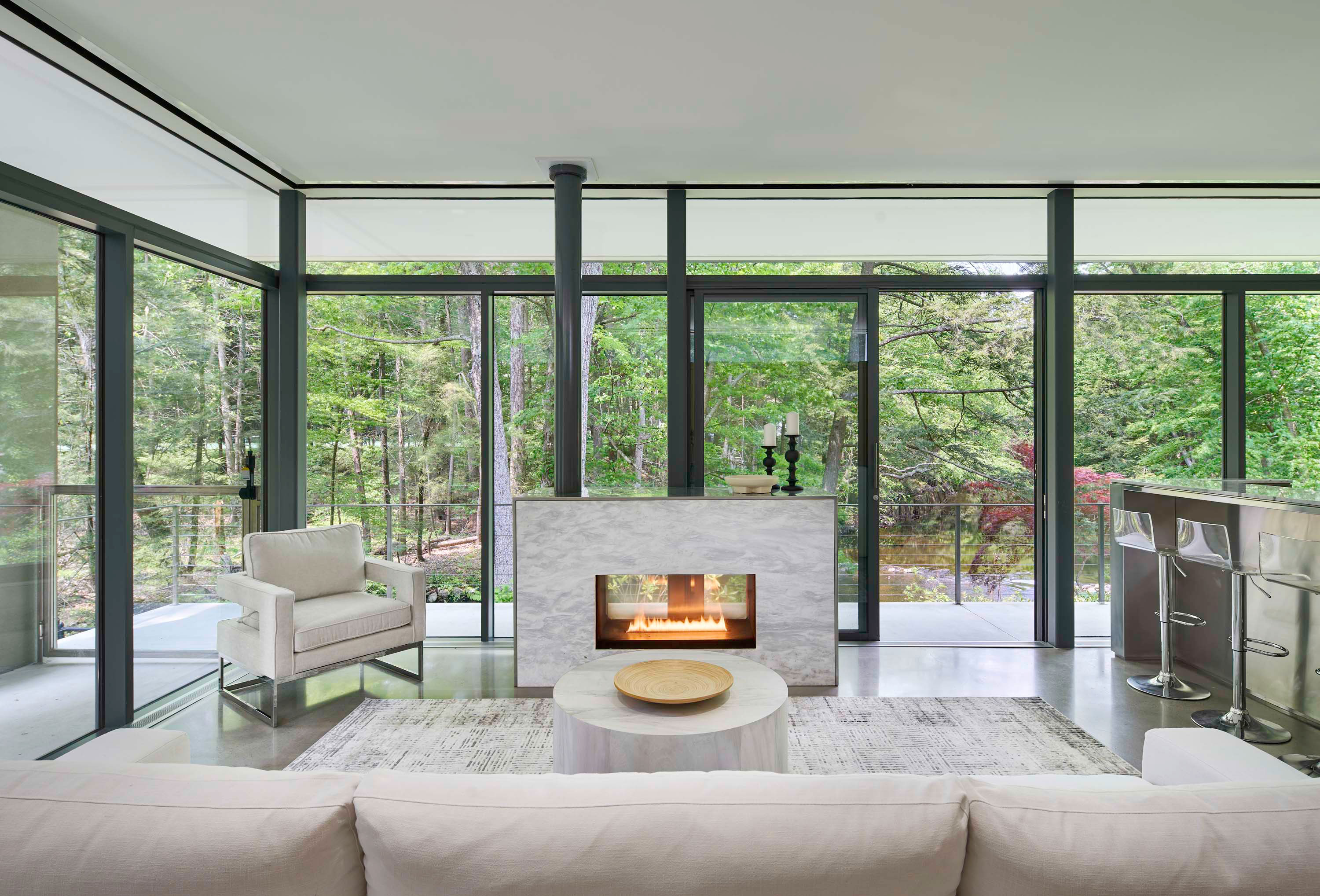 Interior photo of Weston Residence by Specht Novak Architects. Shot by Jasper Lazor, featuring a living space, fireplace, and glass surfaces that with a view of trees around the home.